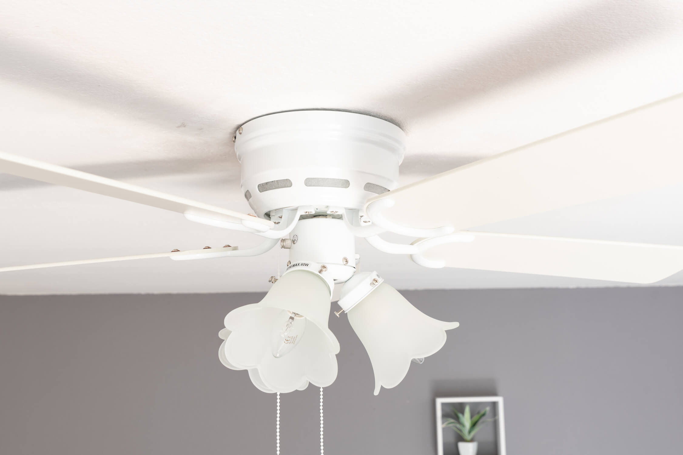 Ventilatore da soffitto bianco con luci. Il soffitto è bianco e lo sfondo grigio.