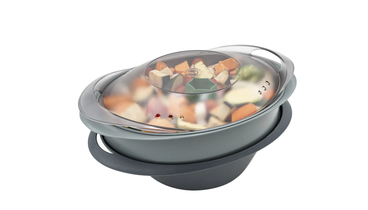 Vaporiera con verdure all'interno, coperchio in plastica. Base grigia, sfondo bianco.