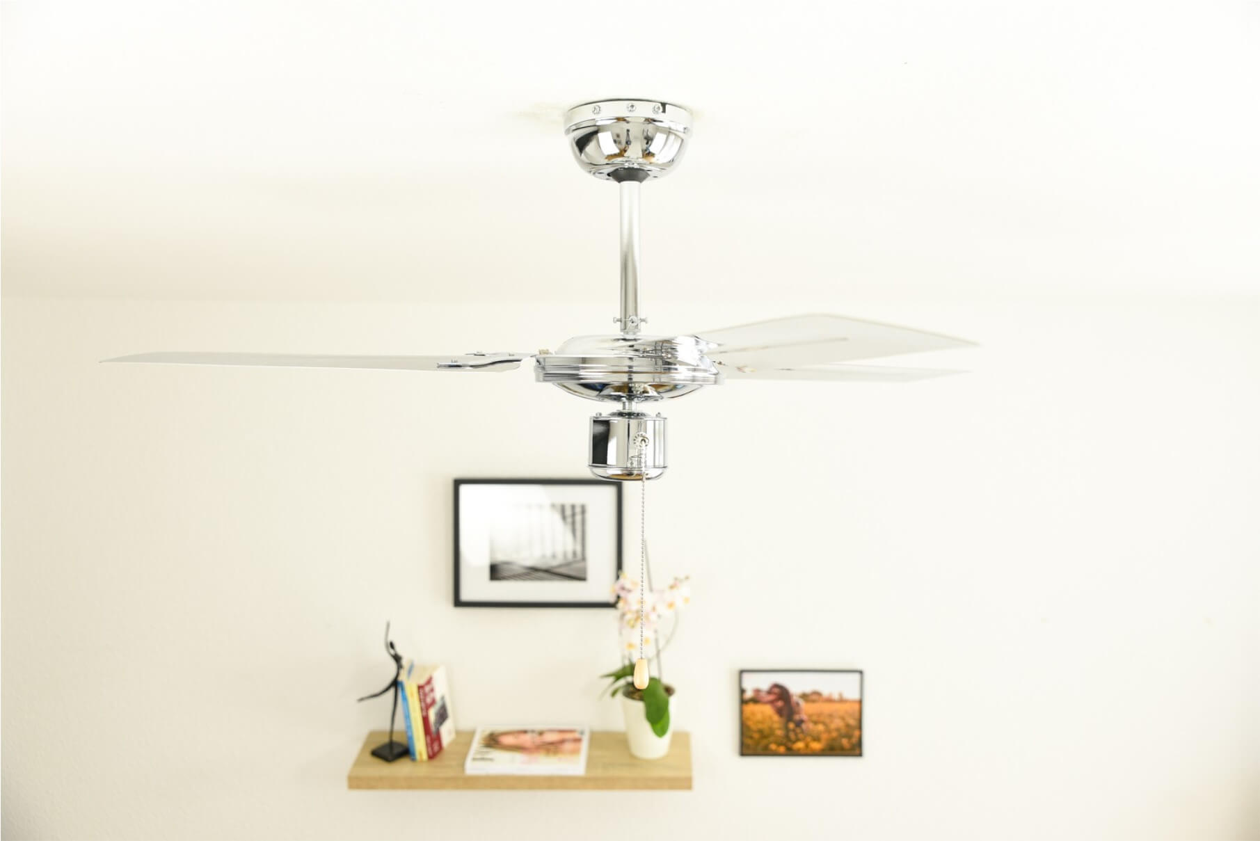 Glänzender silberner Deckenventilator mit 4 Flügeln, mit Leuchte. Wand mit Deko.
