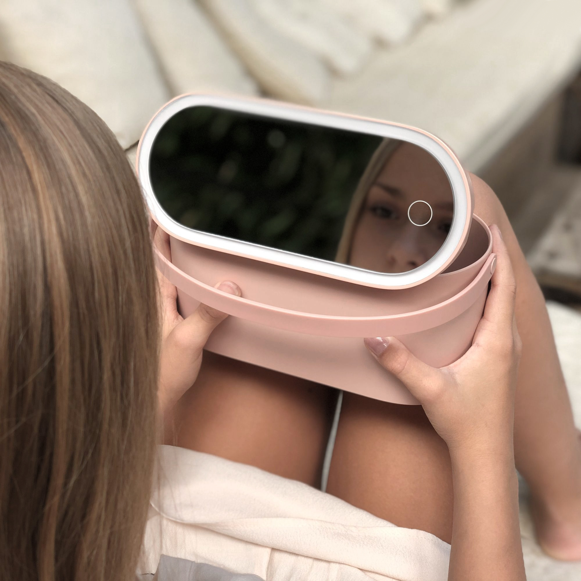 Frau hält einen rosa Spiegel mit Licht, blickt sich an, unscharfer Hintergrund.