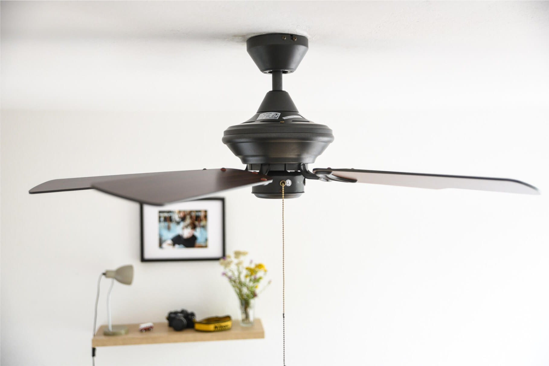 Deckenventilator mit vier dunkelbraunen Flügeln, weiße Decke und Dekoration.
