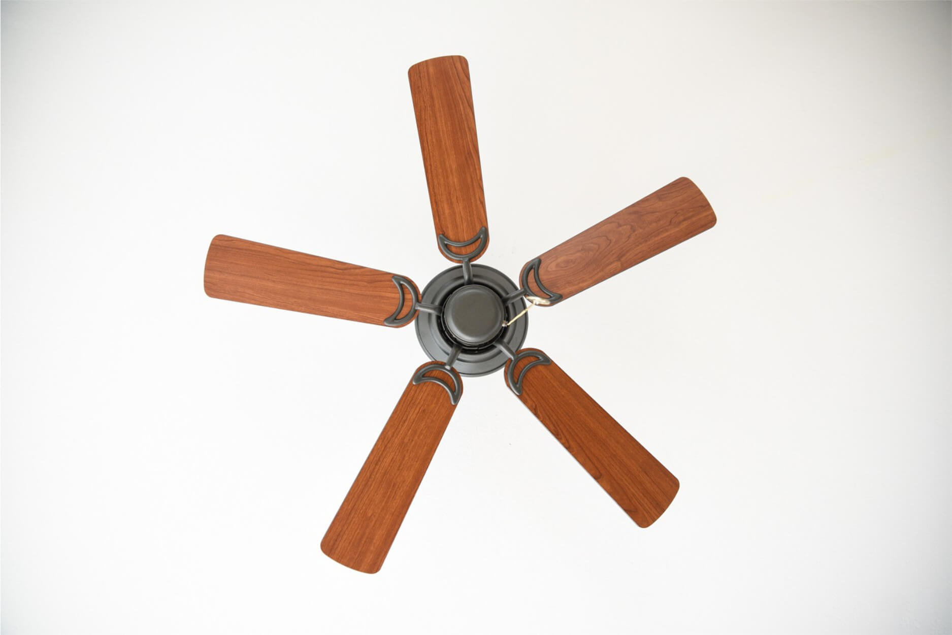 Ein Deckenventilator mit fünf Holzblättern, montiert an einer weißen Decke, von unten betrachtet.