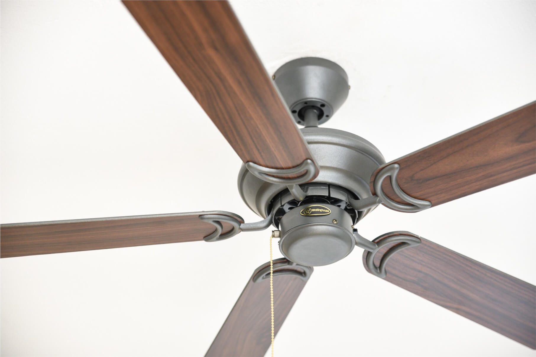 Ein Deckenventilator mit braunen Holzflügeln und einem bronzefarbenen Motor. Der Hintergrund ist weiß.