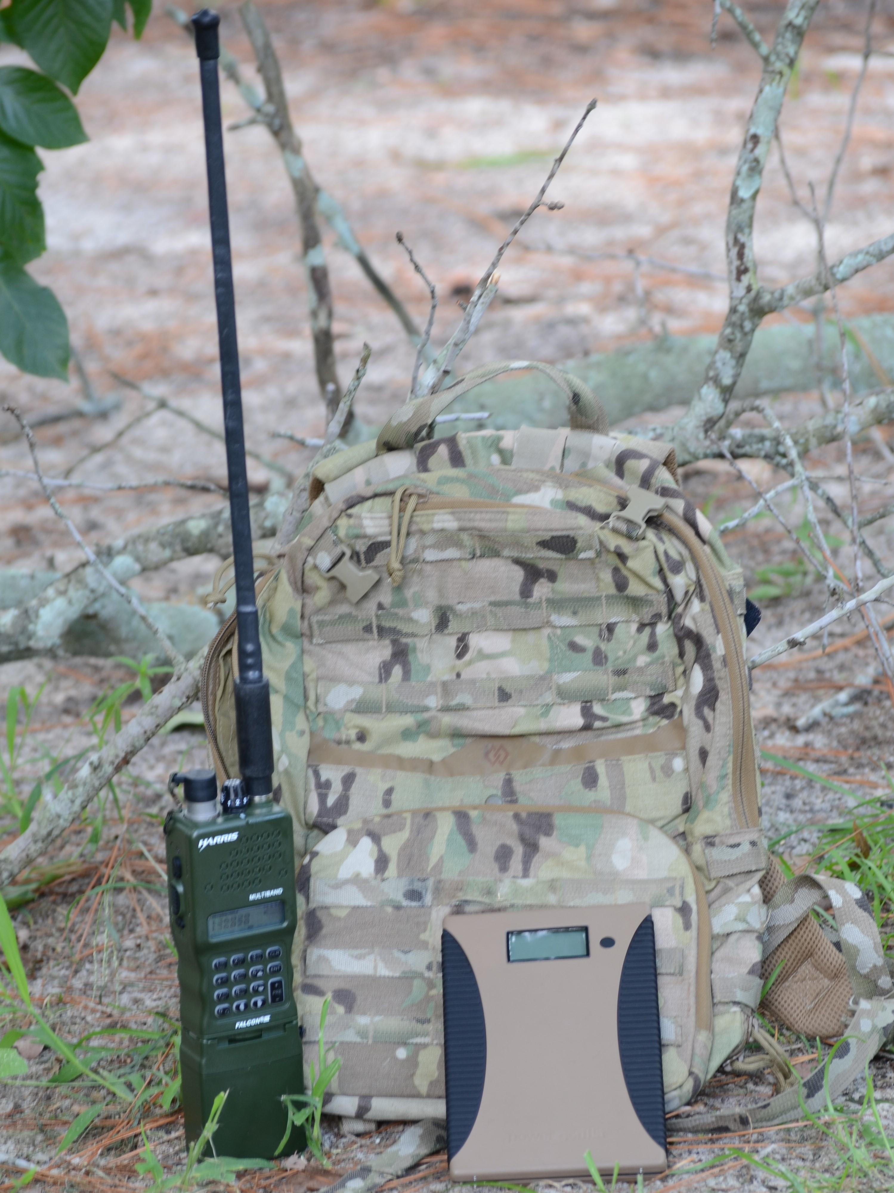 Zaino mimetico con antenna, radio e dispositivo beige, all'aperto.