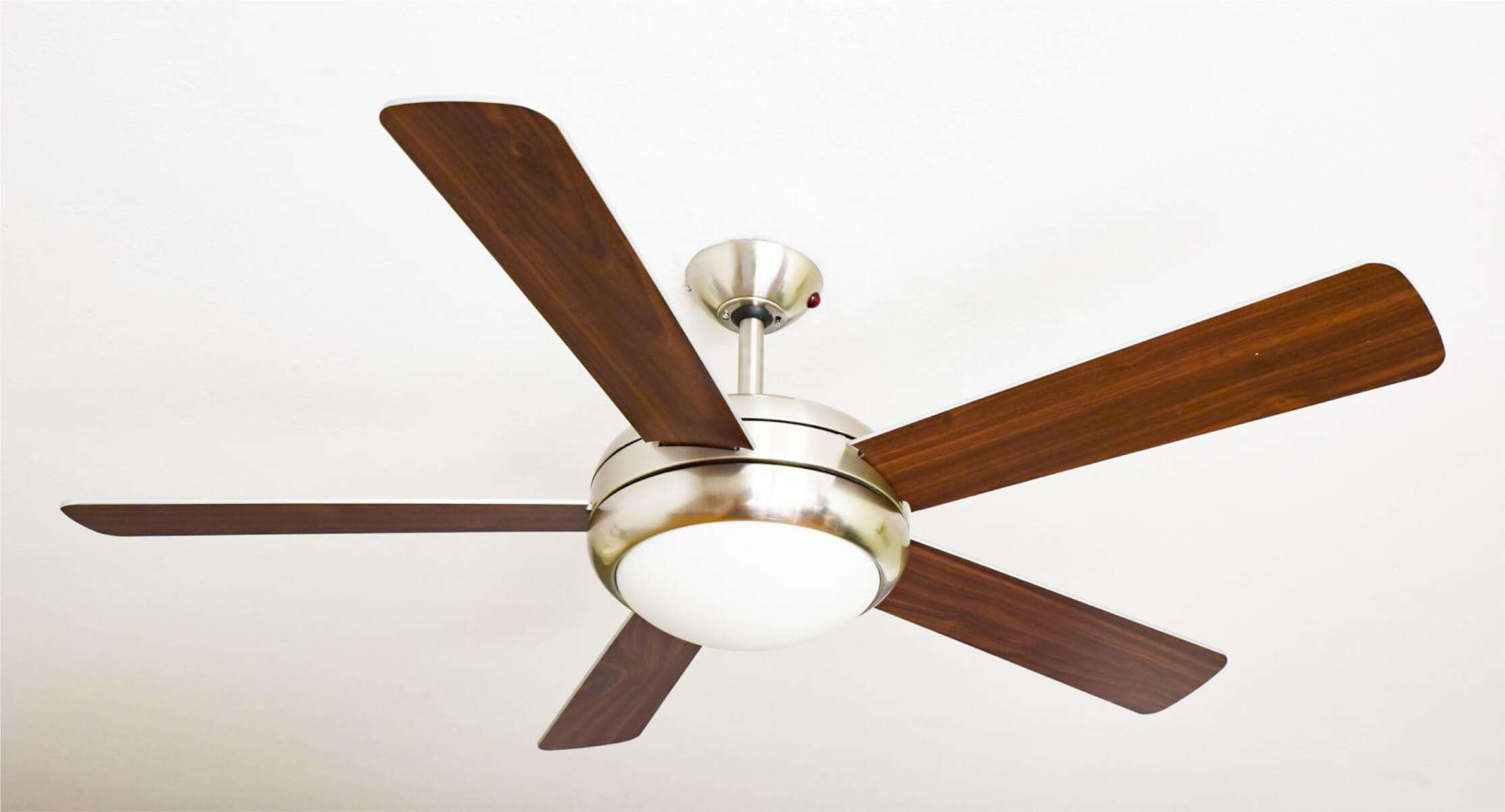 Deckenventilator mit fünf dunklen Holzflügeln und einer weißen Leuchte.