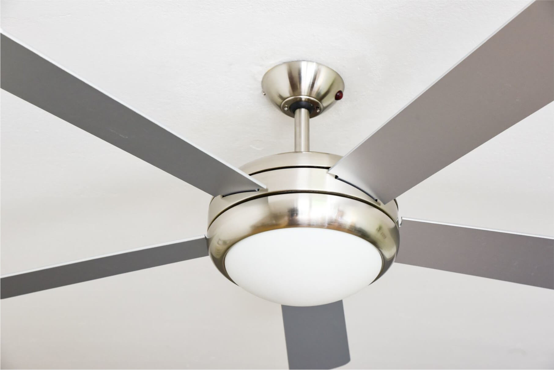 Ein Deckenventilator mit fünf grauen Flügeln und einem weißen Licht. Der Ventilator ist silberfarben.
