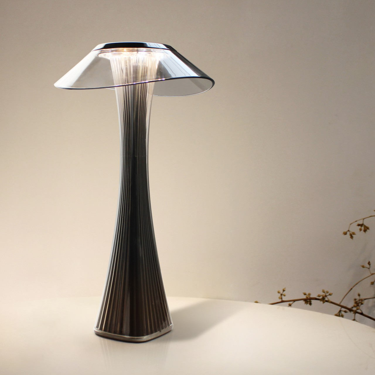 Eine moderne Lampe mit grauem Schirm steht auf weißem Tisch, vor hellem Hintergrund.