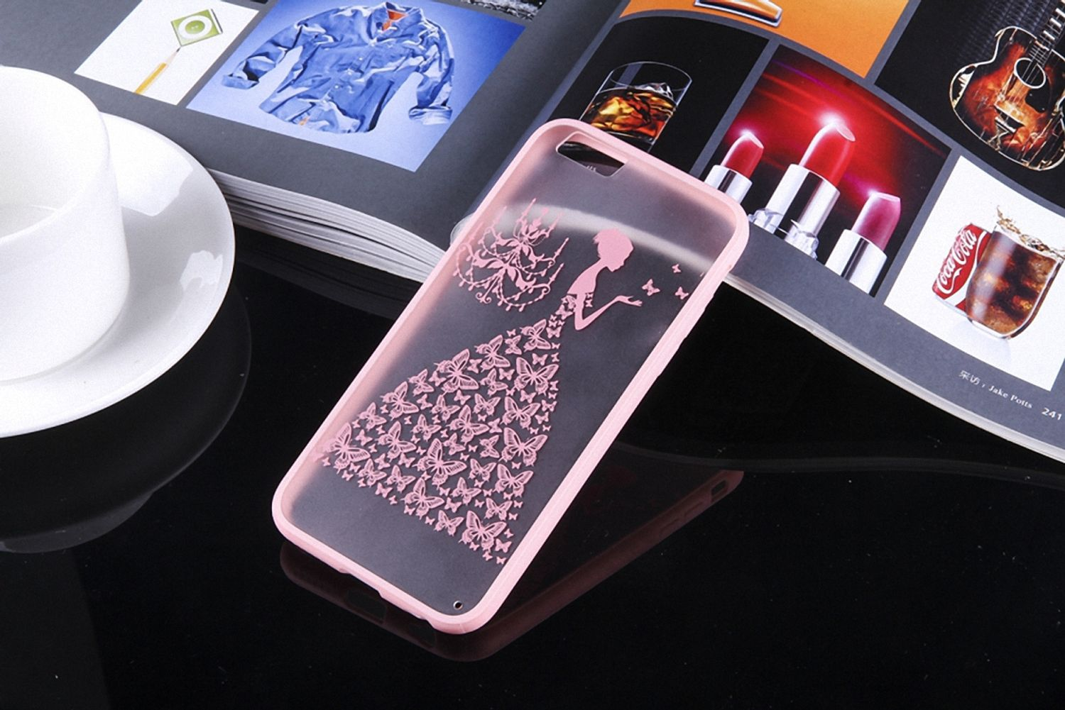 Eine rosa Handyhülle mit einem Schmetterlingskleid-Design. Sie liegt auf einer glänzend schwarzen Oberfläche.