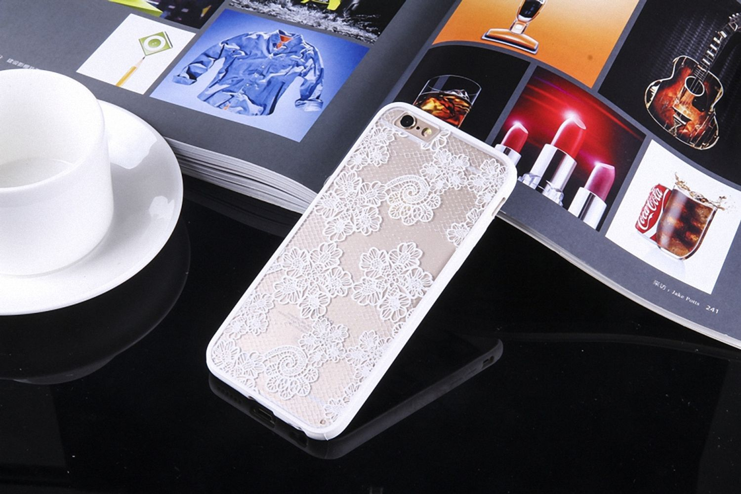 Handyhülle mit weißem Spitzendesign auf glänzender Oberfläche mit Tasse und Magazin.