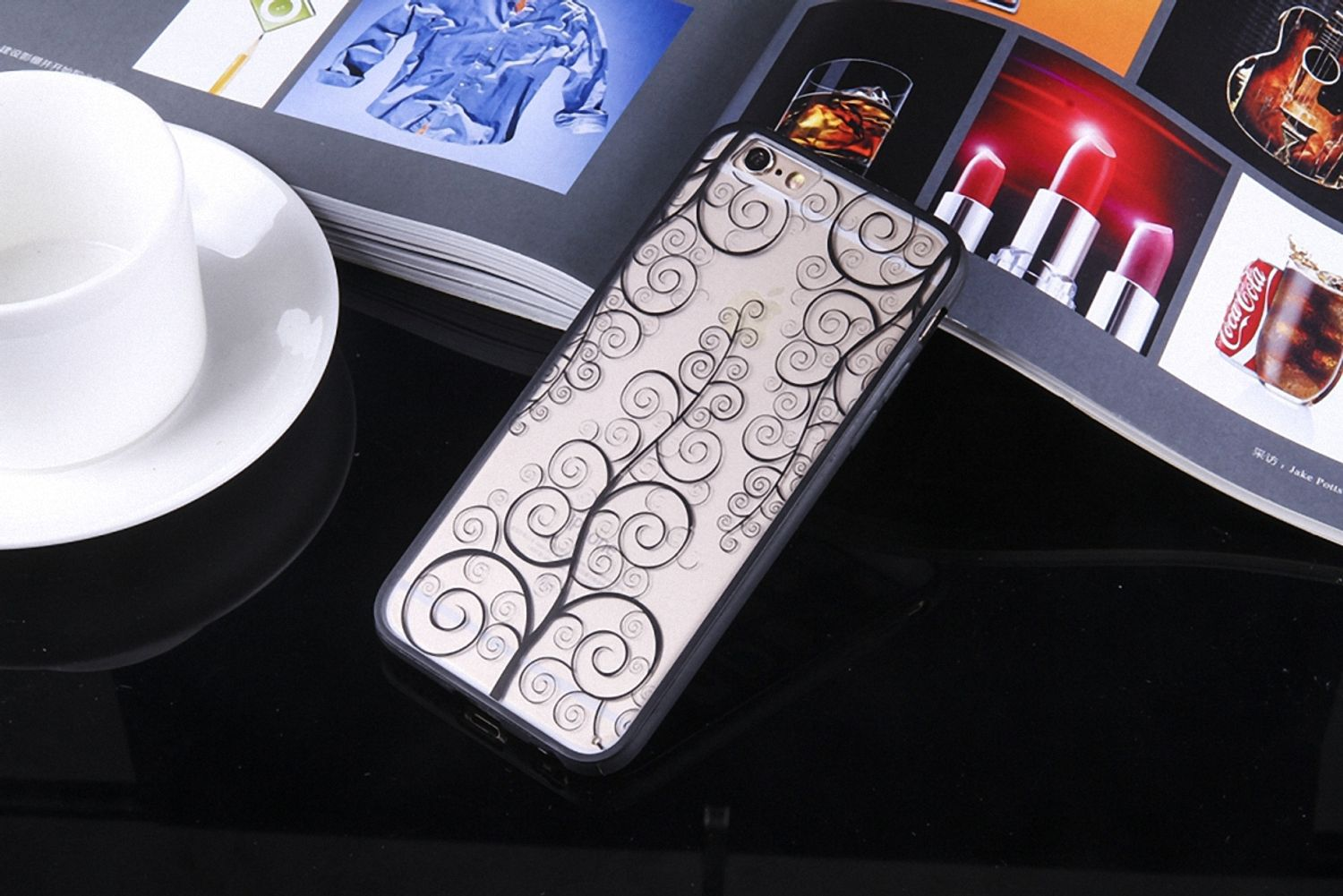 Handyhülle mit Wirbeldesign auf reflektierender Oberfläche, neben einer Tasse und einer Zeitschrift.