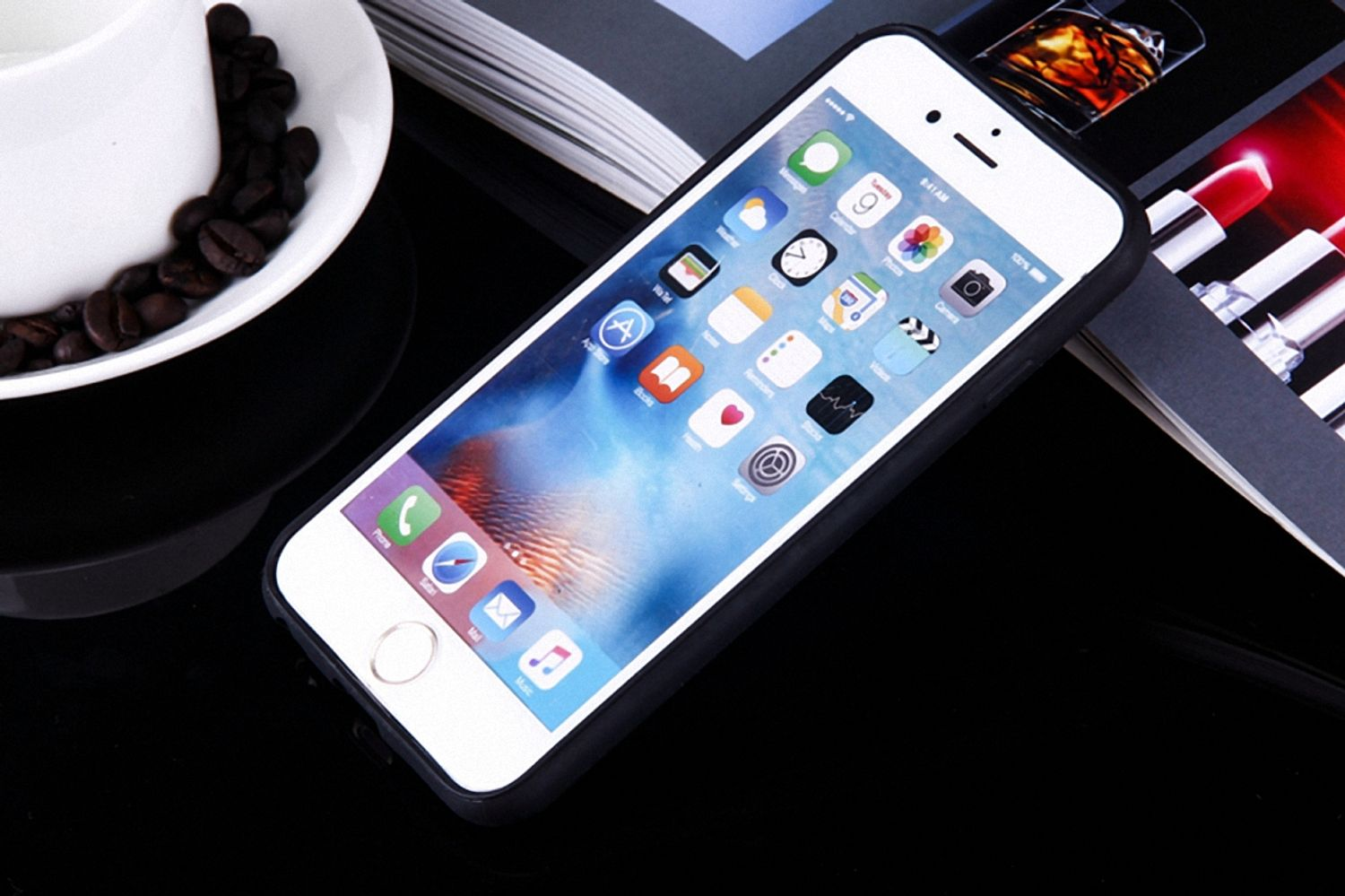 Ein Smartphone mit schwarzer Hülle liegt auf glänzender Oberfläche neben einer Zeitschrift und Kaffeebohnen.