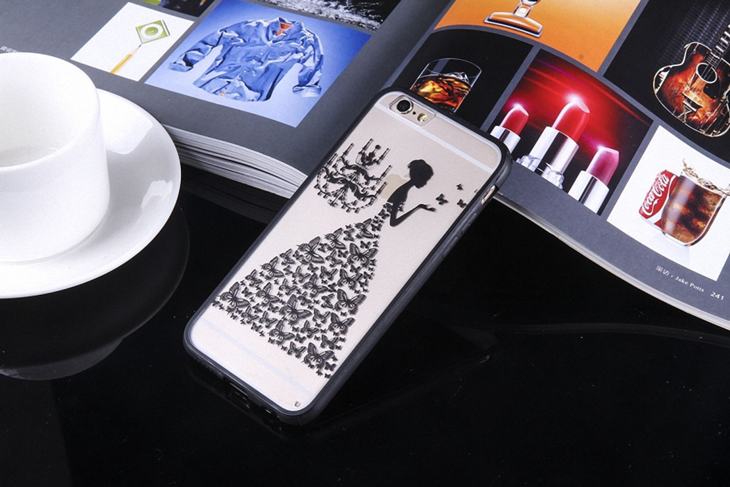 iPhone in einer Hülle mit einem Design eines Kleides mit Schmetterlingen auf einem Tisch mit Zeitschriften und einer Tasse.