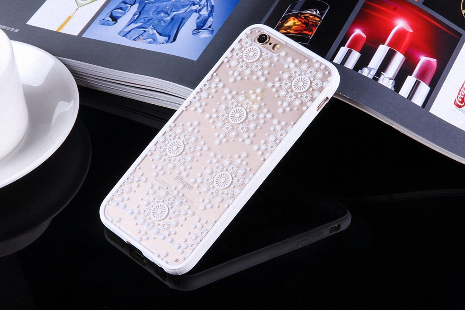 Weißes Handycase mit floralem Design auf reflektierender Oberfläche, mit Zeitschriftenhintergrund.