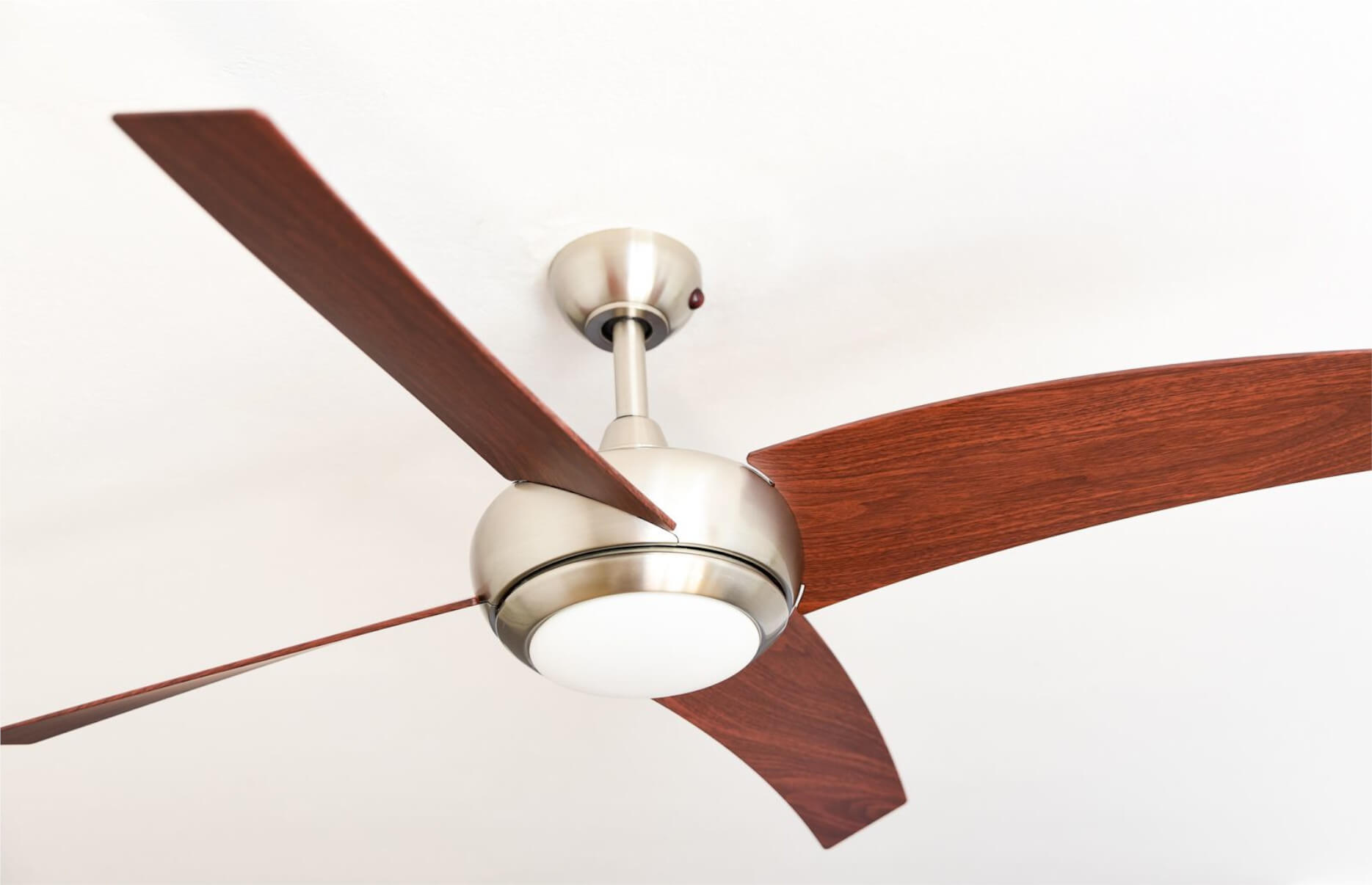 Deckenventilator mit braunen Flügeln und silbernem Motor, weißer Decke im Hintergrund.