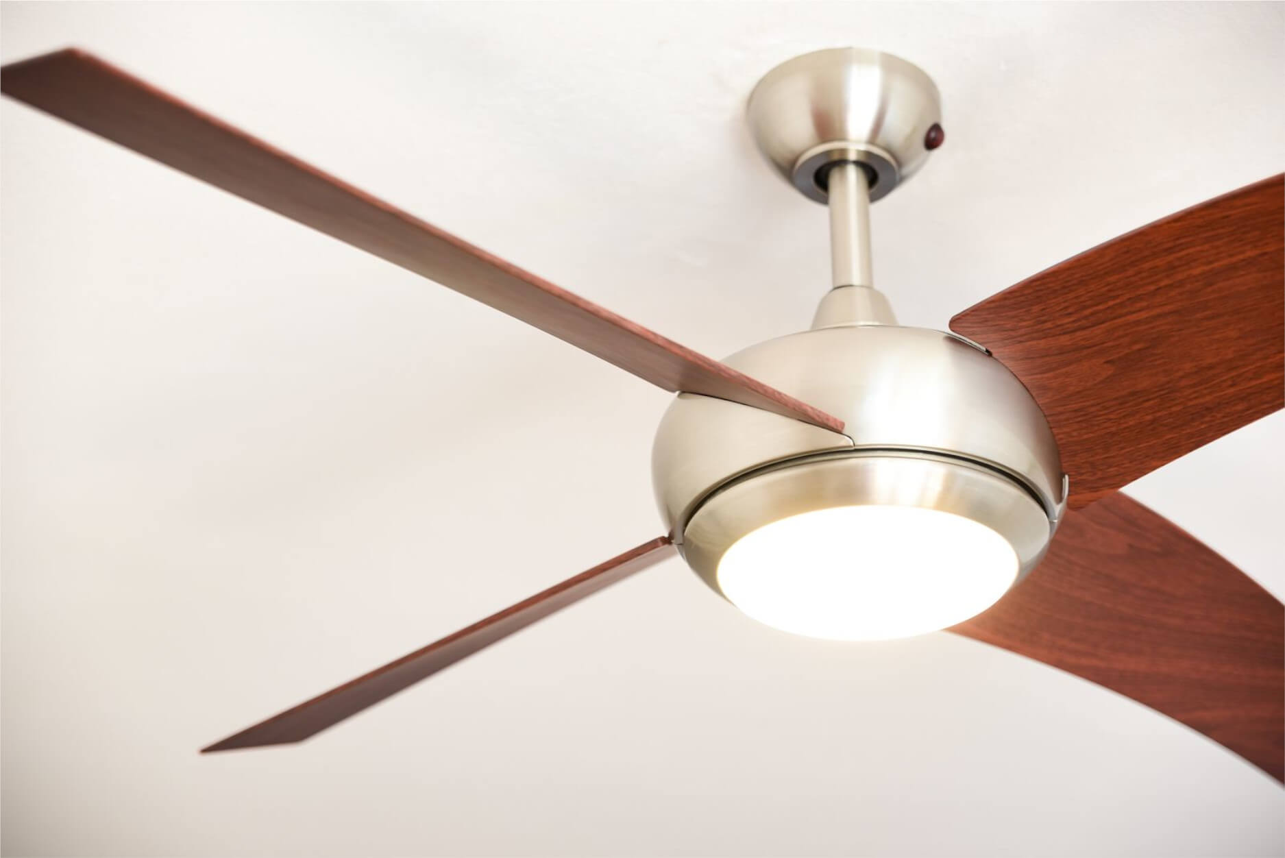 Ein Deckenventilator mit Holzflügeln und Licht. Der Hintergrund ist weiß.