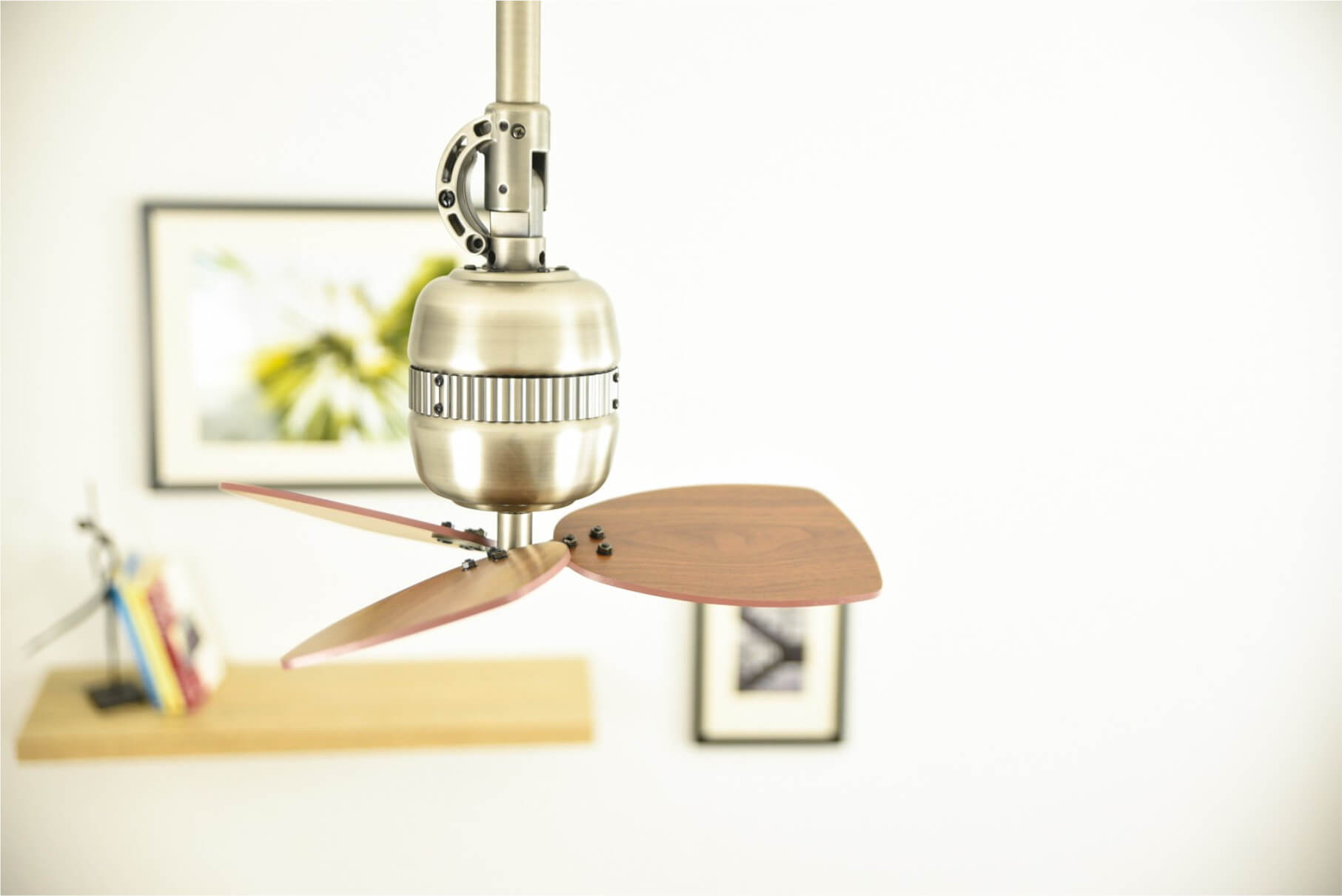Ventilatore a soffitto con pale in legno, motore argentato e sfondo chiaro con decorazioni.