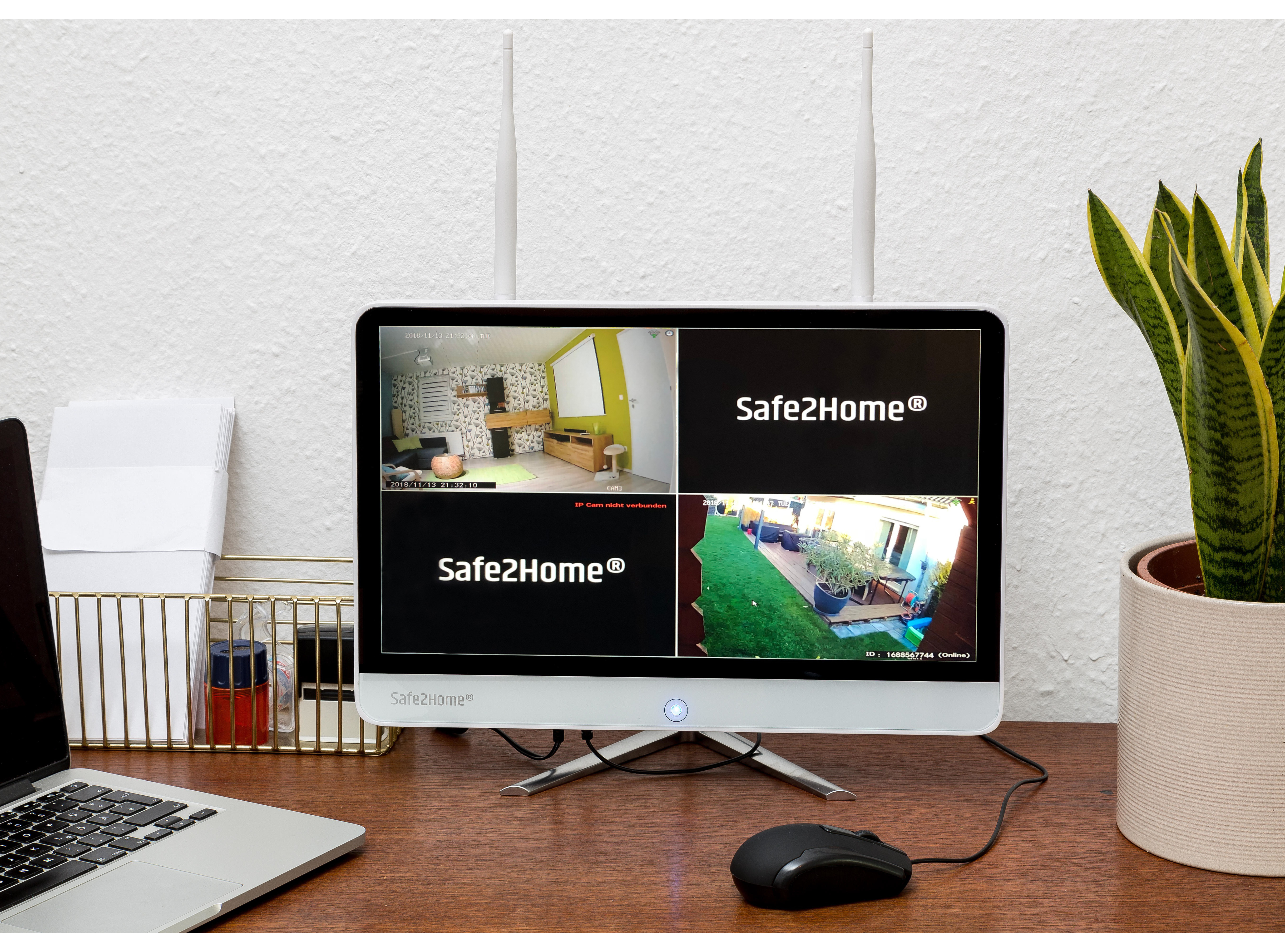 Sicherheitsmonitor mit mehreren Kameraansichten, auf einem Schreibtisch mit Laptop und Pflanze.