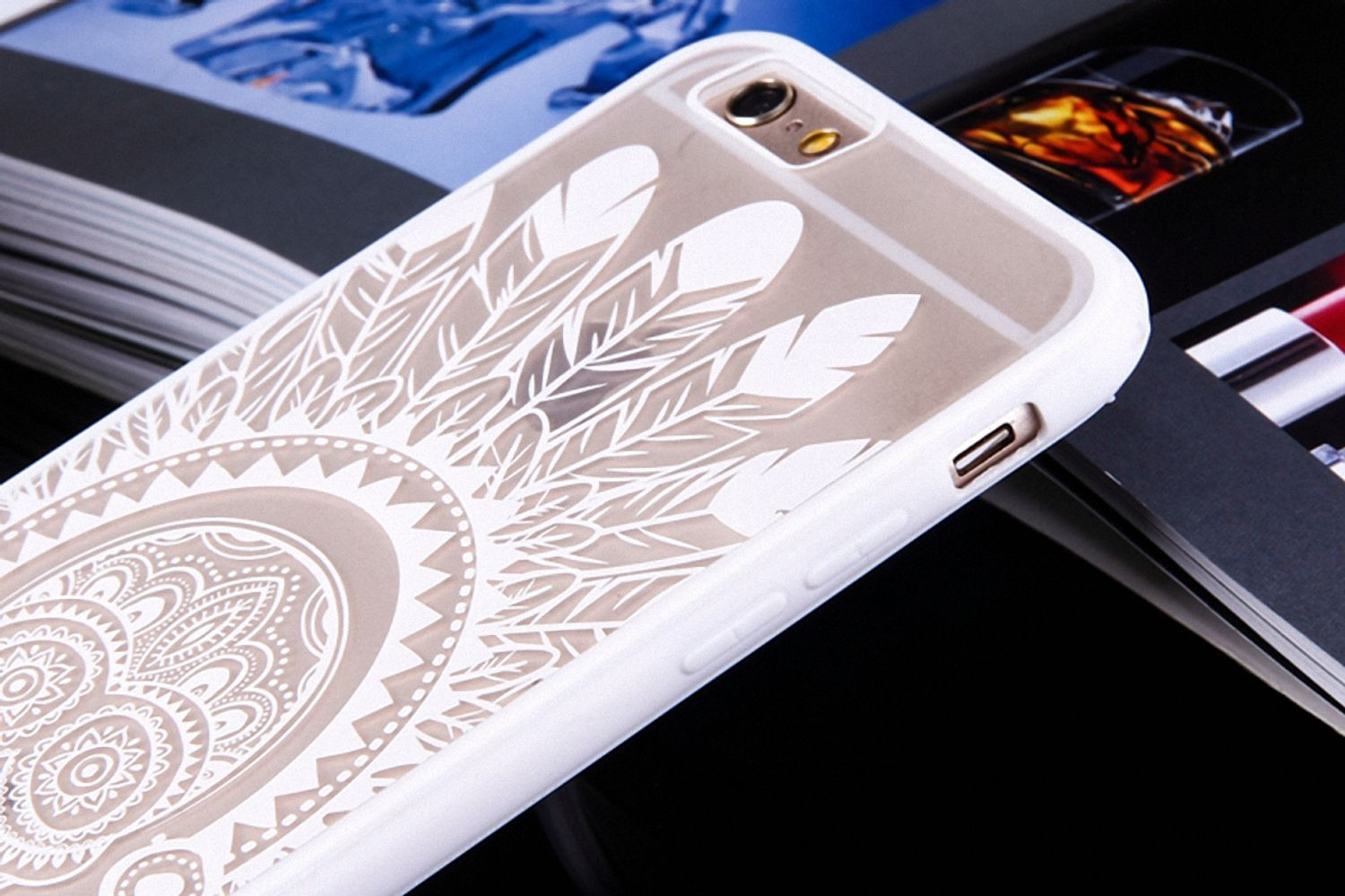 Weiße Handyhülle mit Feder- und Mandala-Design, auf einer Zeitschrift, Nahaufnahme.