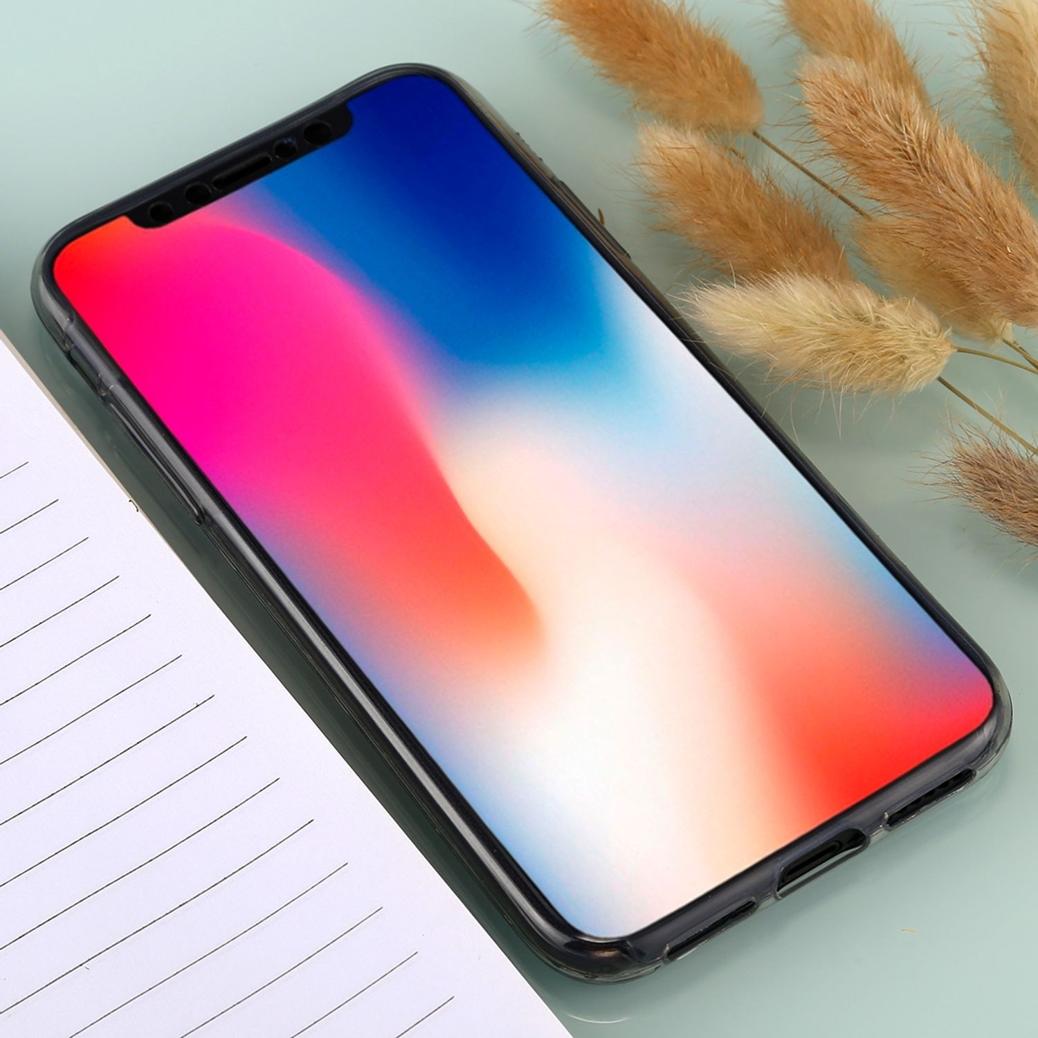 Telefon mit buntem, abstraktem Hintergrundbild, Notizbuch und getrockneten Blumen.