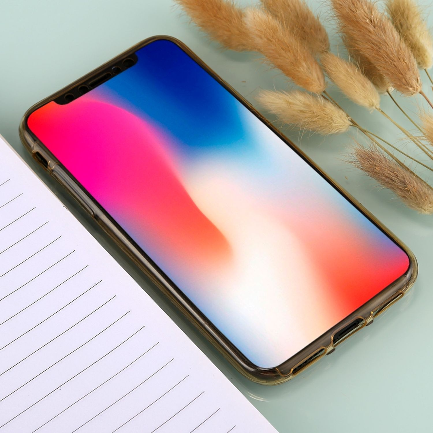 Telefon in Hülle mit farbenfrohem Gradienten-Hintergrund, Notizbuch und getrockneten Blumen daneben.
