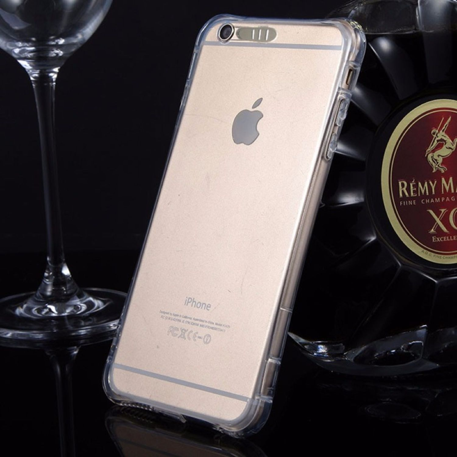 Eine transparente Handyhülle auf einem goldenen iPhone. Das Telefon befindet sich in der Nähe eines Glases und einer Alkoholflasche.