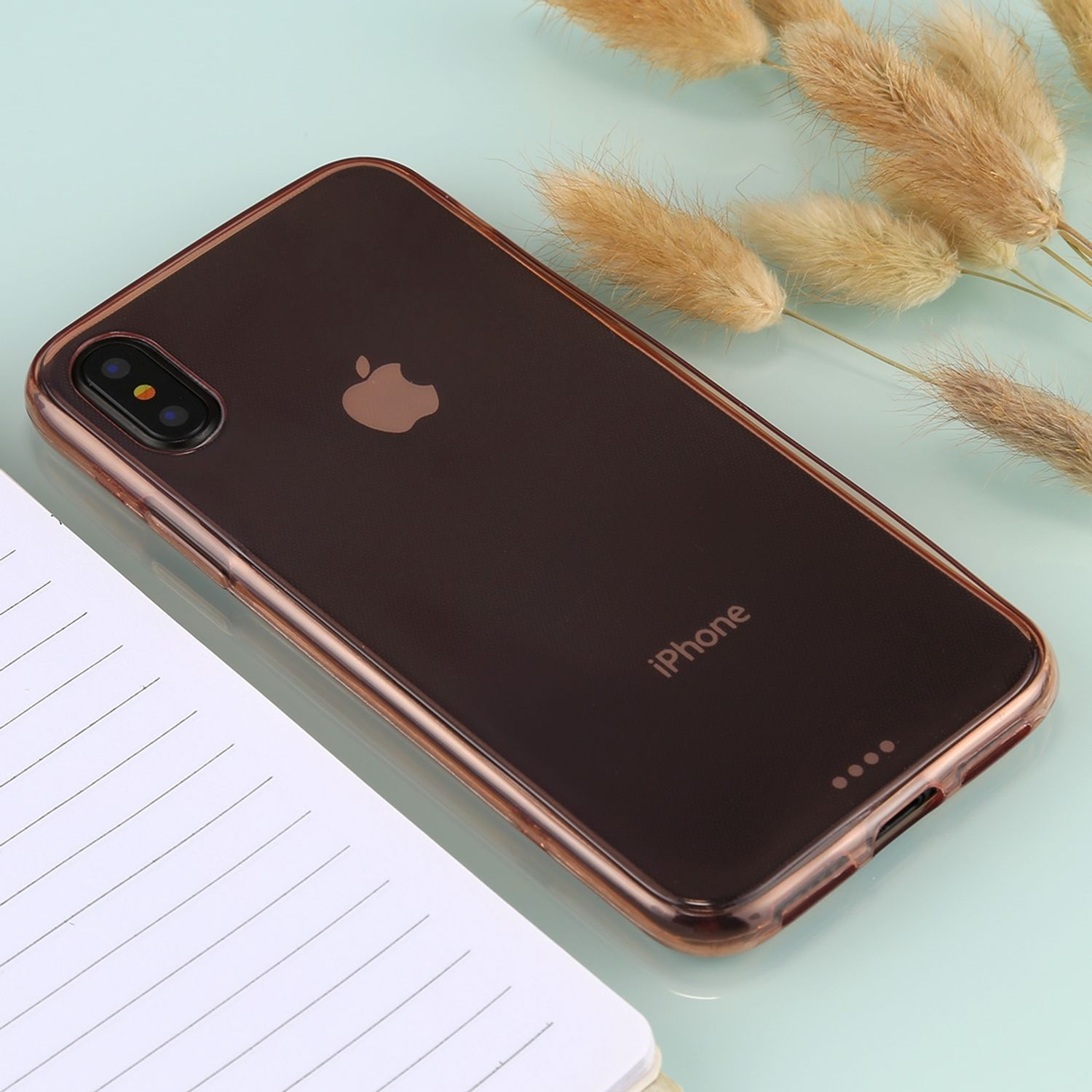 Eine Handyhülle für ein iPhone mit dem Wort iPhone darauf. Es gibt ein weißes Notizbuch und Blumen.