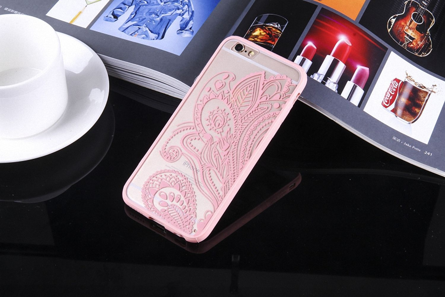 Eine rosa gemusterte Handyhülle auf einer reflektierenden Oberfläche neben einer Zeitschrift und Tasse.