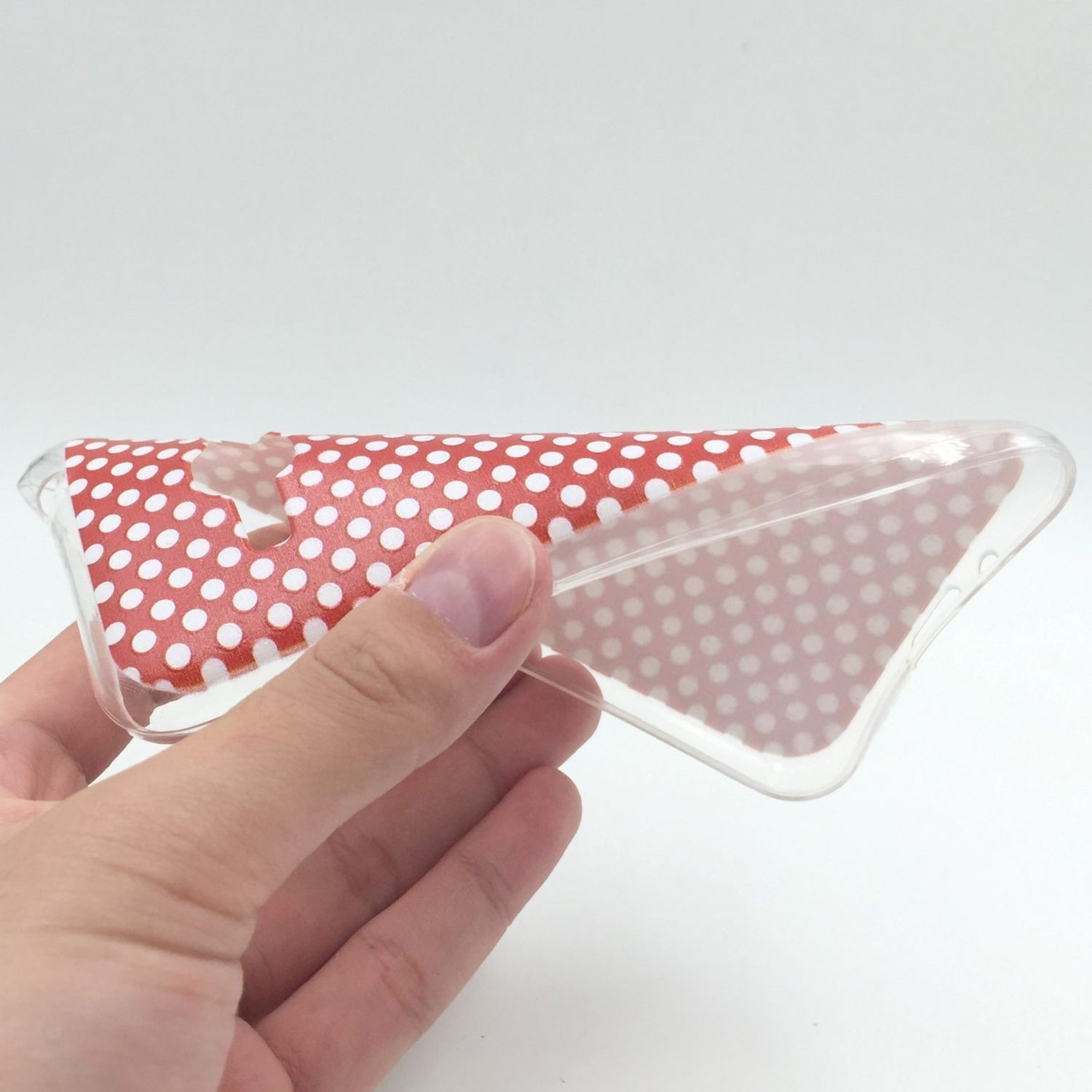 Hand hält durchsichtige Handyhülle mit rotem Polka-Dot-Design.