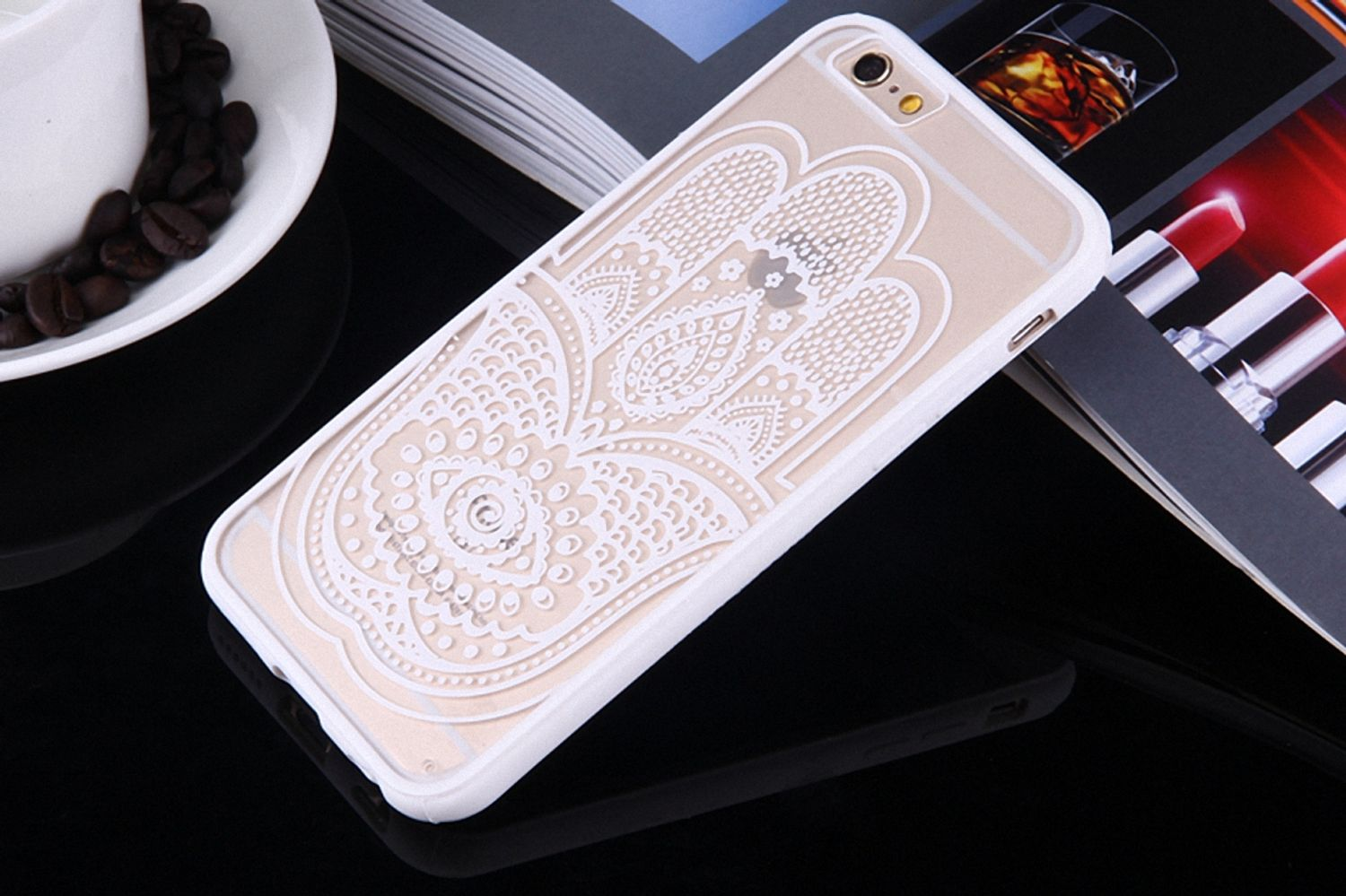 Klare Handyhülle mit weißem Hamsa-Design auf reflektierender Oberfläche. Kaffeetasse und Bohnen im Hintergrund sichtbar.