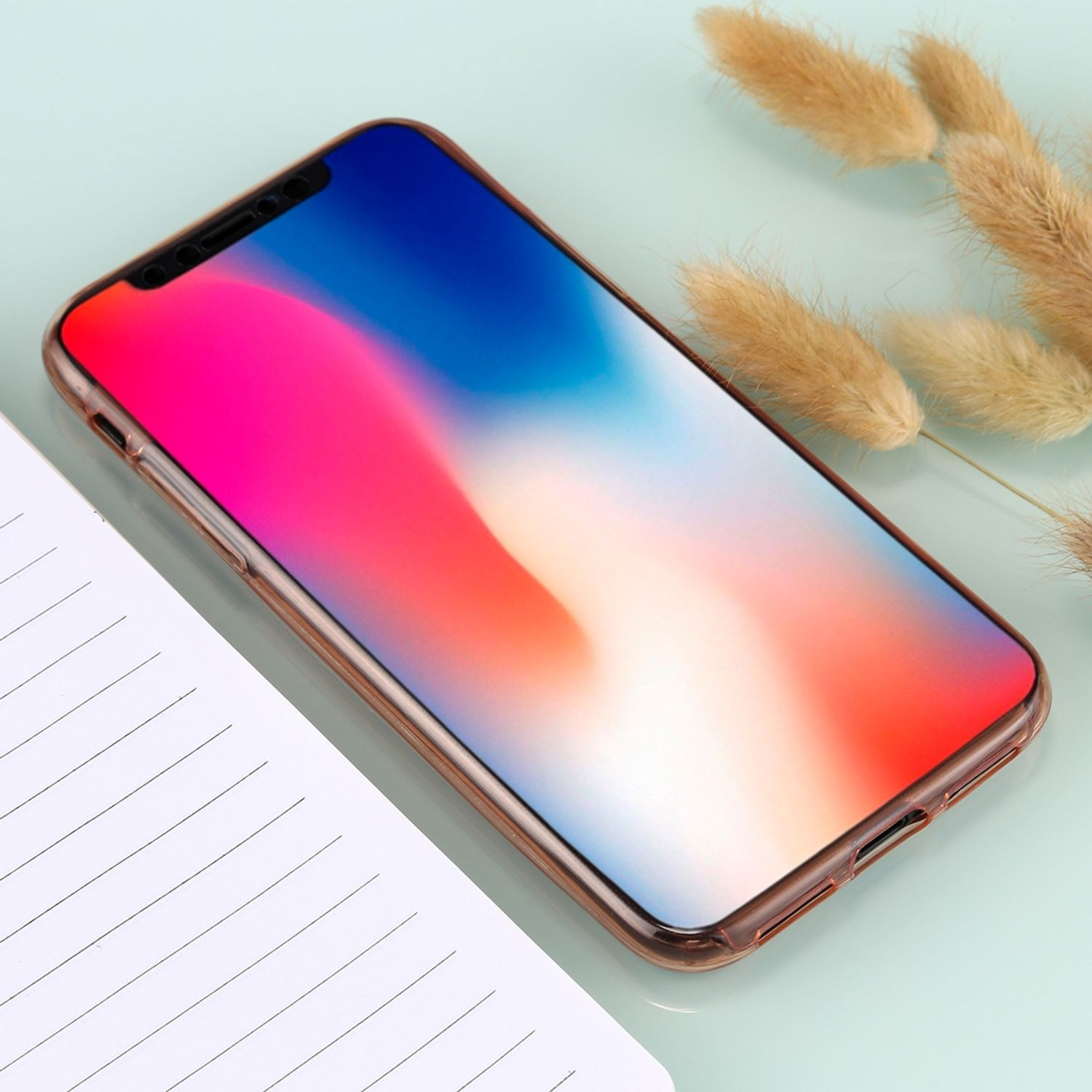 Ein Telefon mit farbenfrohem Bildschirm liegt auf einer hellblauen Oberfläche neben einem Notizblock und Trockenblumen.