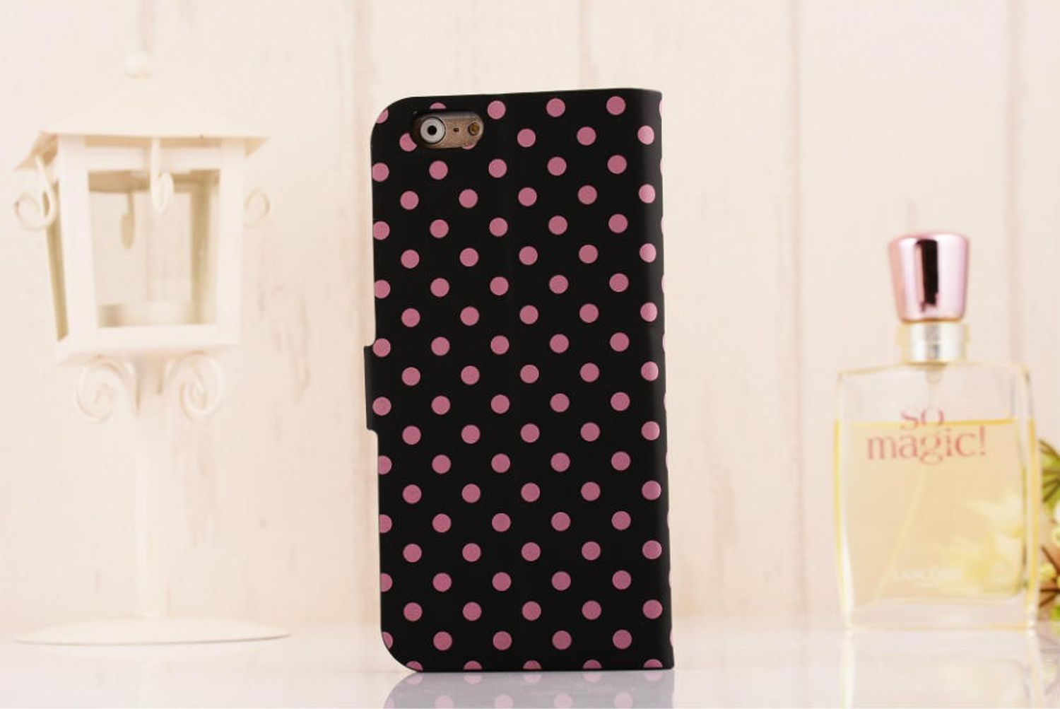 Eine schwarze Handyhülle mit rosa Punkten, teilweise geöffnet. Es liegt auf einer Oberfläche mit einer Parfümflasche.