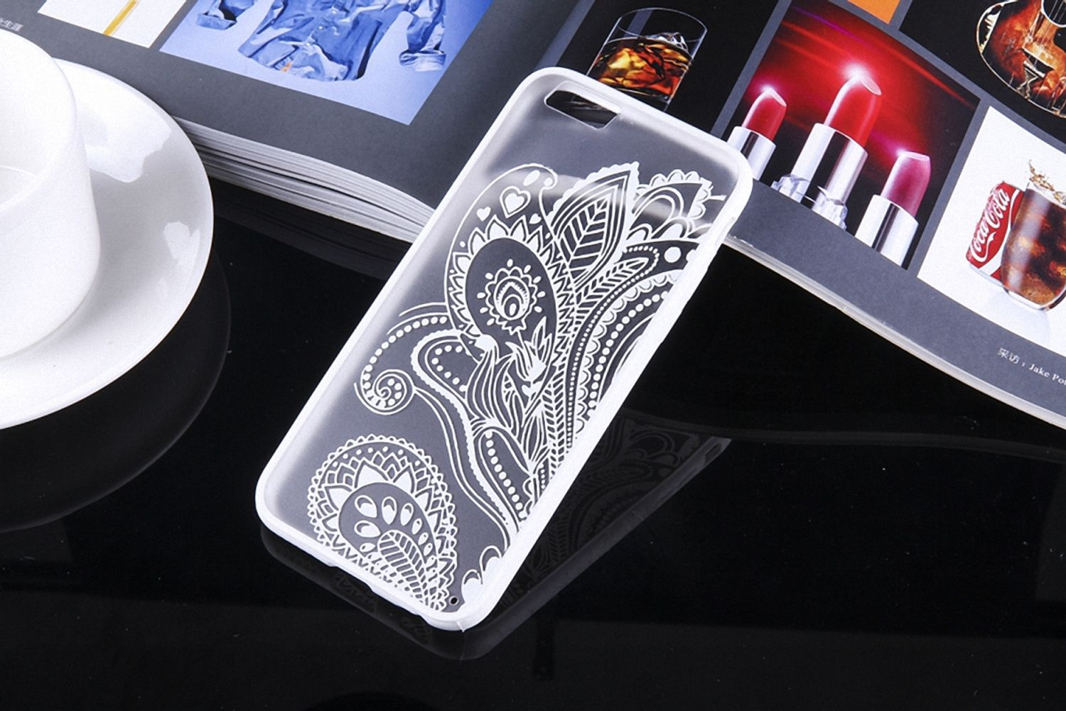 Transparente Handyhülle mit weißem Blumendesign, mit Buch und Gegenständen auf glänzender Oberfläche.