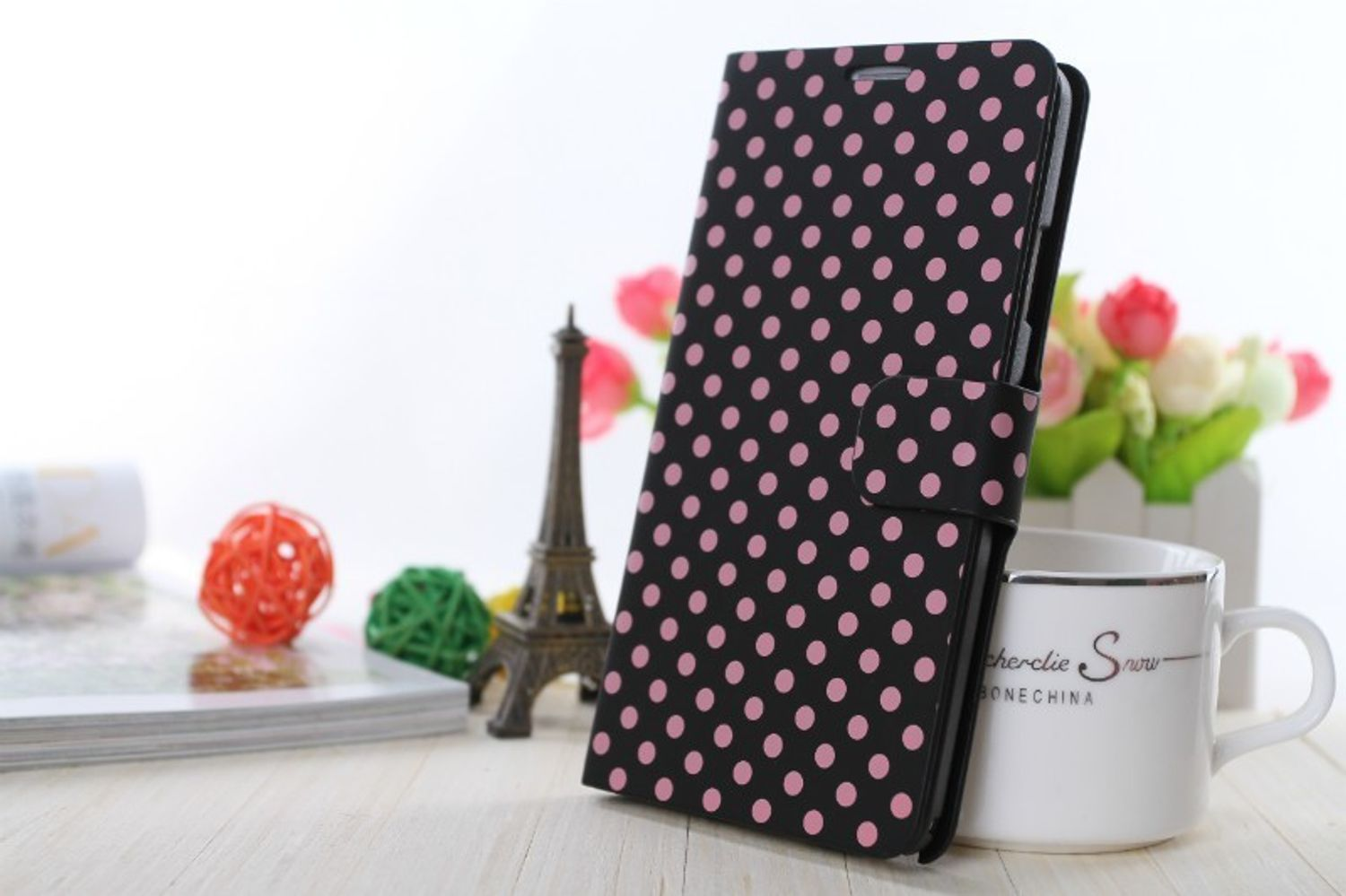 Schwarze Handyhülle mit pinken Punkten, geöffnet. Eiffelturm und Blumen im Hintergrund.