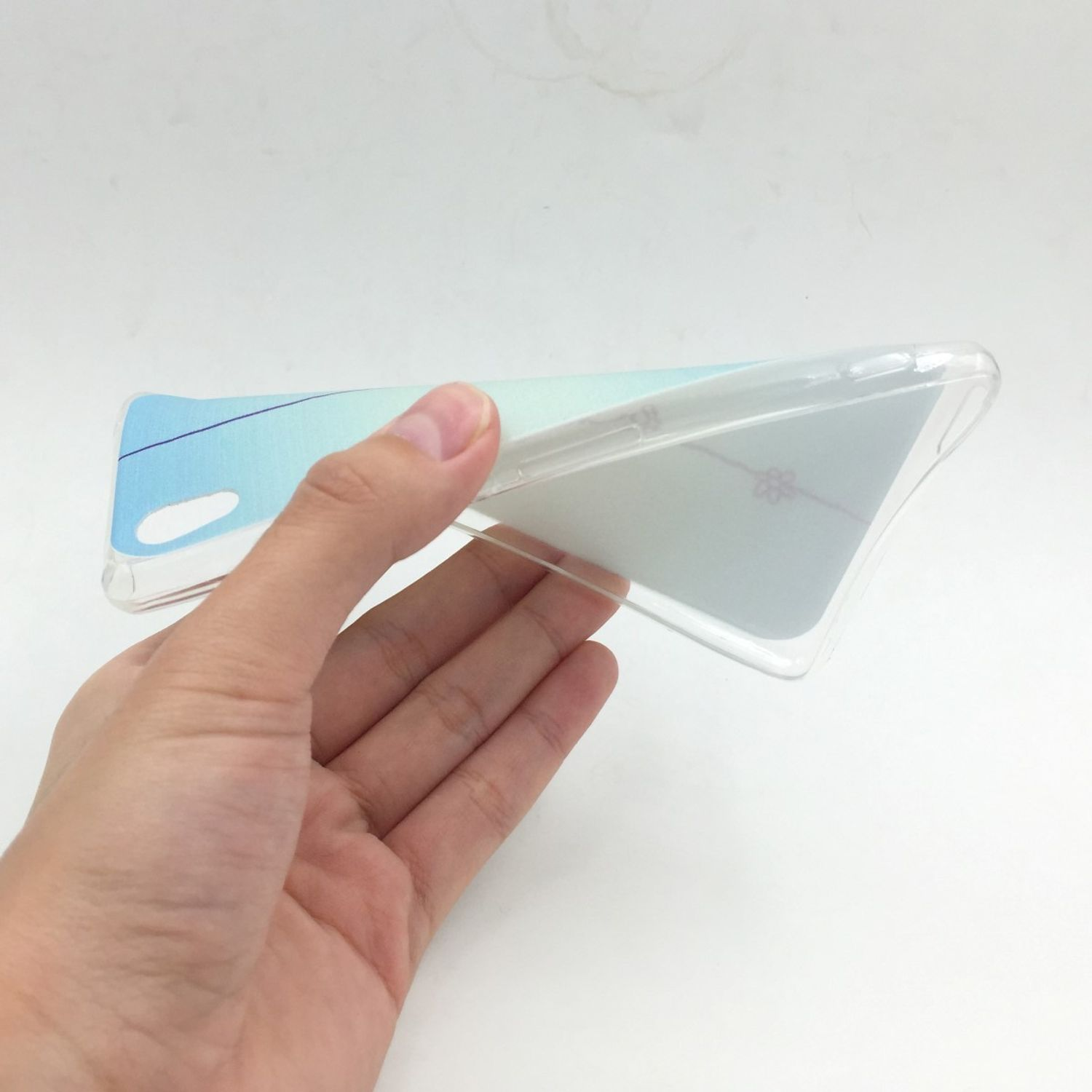 Hand hält eine transparente Handyhülle mit blau-weißem Farbverlauf. Der Hintergrund ist weiß.