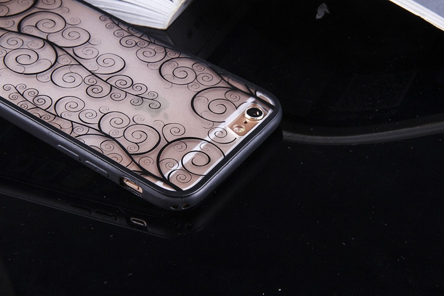 Schwarze Handyhülle mit Wirbeldesign, heller Hintergrund. Telefon rechts, schräge Ansicht.