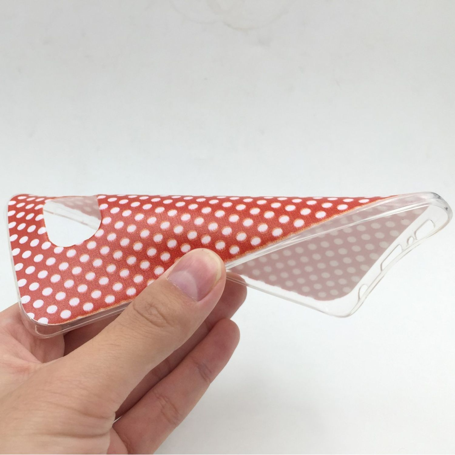 Hand hält eine rot-weiß gepunktete Handyhülle. Transparent innen, weißer Hintergrund.