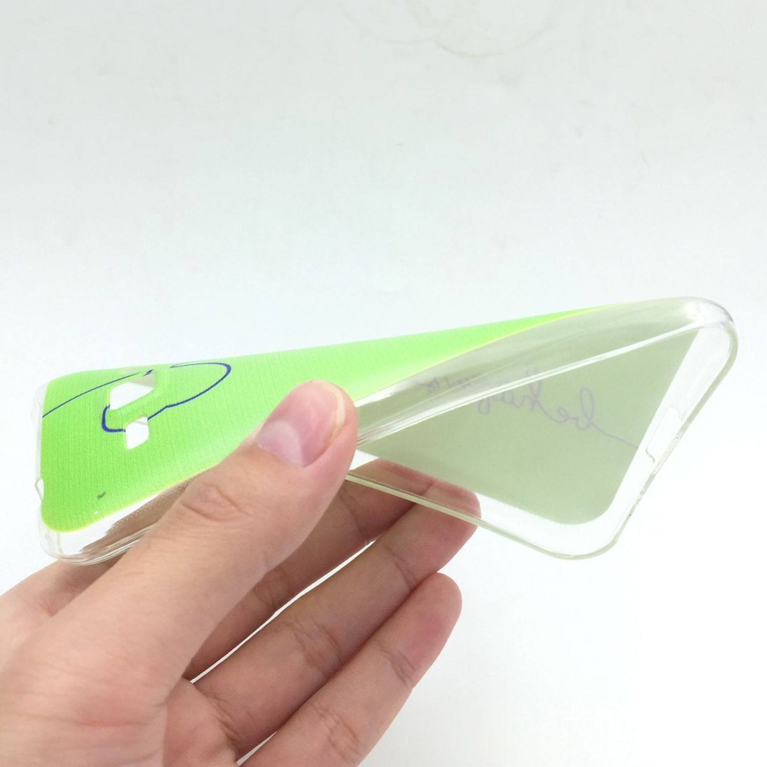 Hand hält eine transparente Handyhülle mit grünem Design. Weißer Hintergrund.