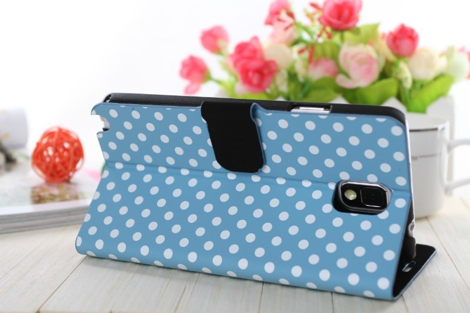 Eine blaue Handyhülle mit weißen Punkten. Blumen im Hintergrund.