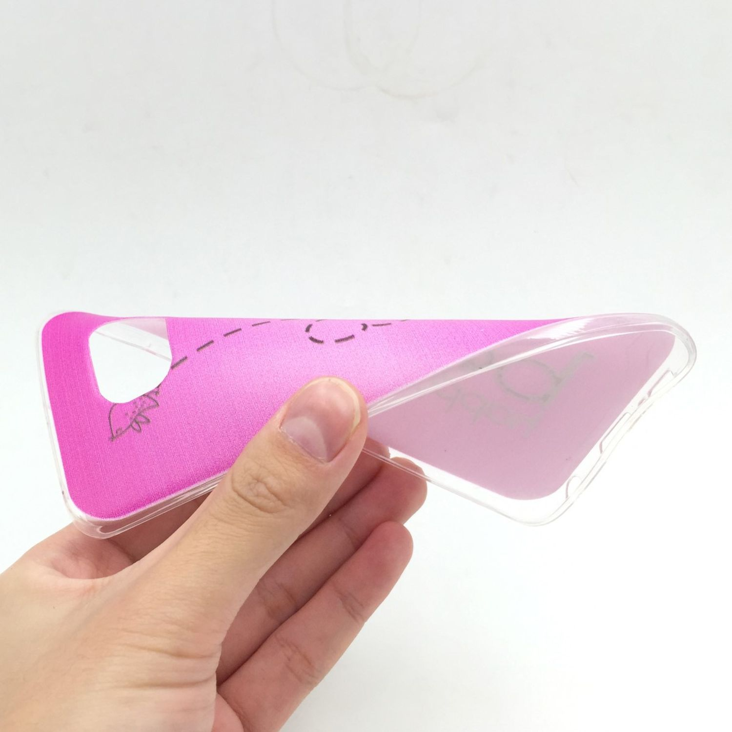 Hand hält eine pinkfarbene Handyhülle mit Design. Hintergrund ist eine weiße Oberfläche.