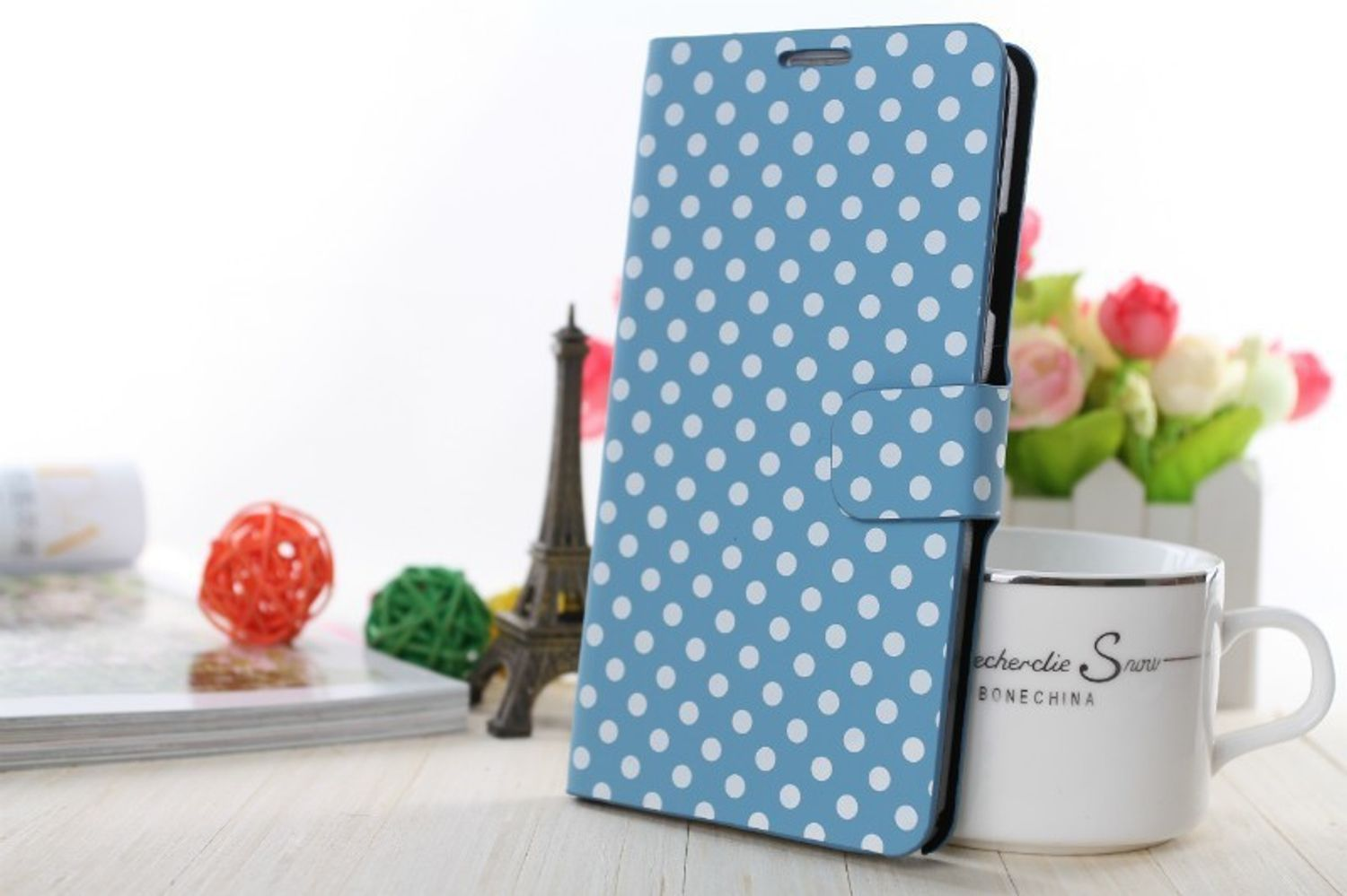 Blaue Handyhülle mit weißen Punkten, neben einer Tasse und einem Eiffelturm-Modell.