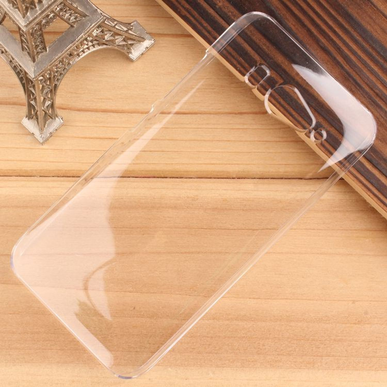 Eine transparente Handyhülle auf einer Holzoberfläche, mit einem Eiffelturm-Modell im Hintergrund.
