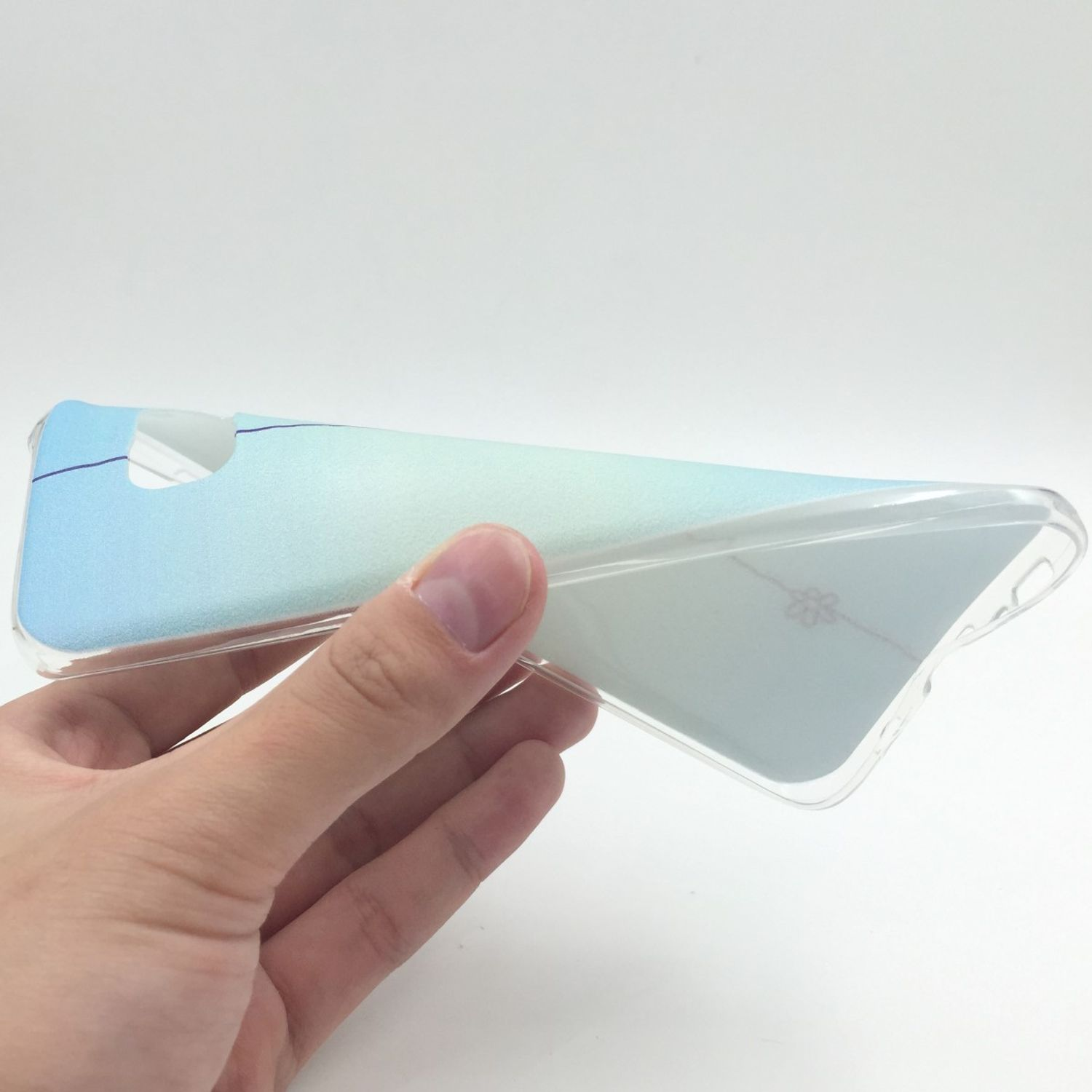 Hand hält eine transparente Handyhülle. Sie hat ein hellblaues und weißes Gradientendesign.