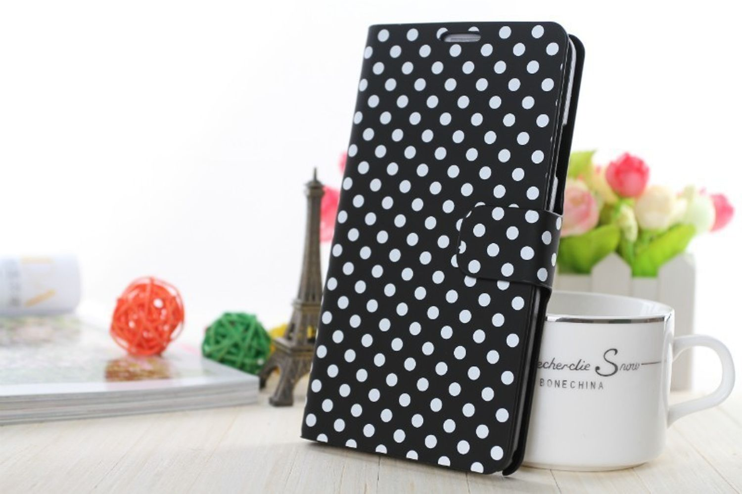 Schwarze Handyhülle mit weißen Polka-Dots, geschlossen, neben Eiffelturm-Dekor.