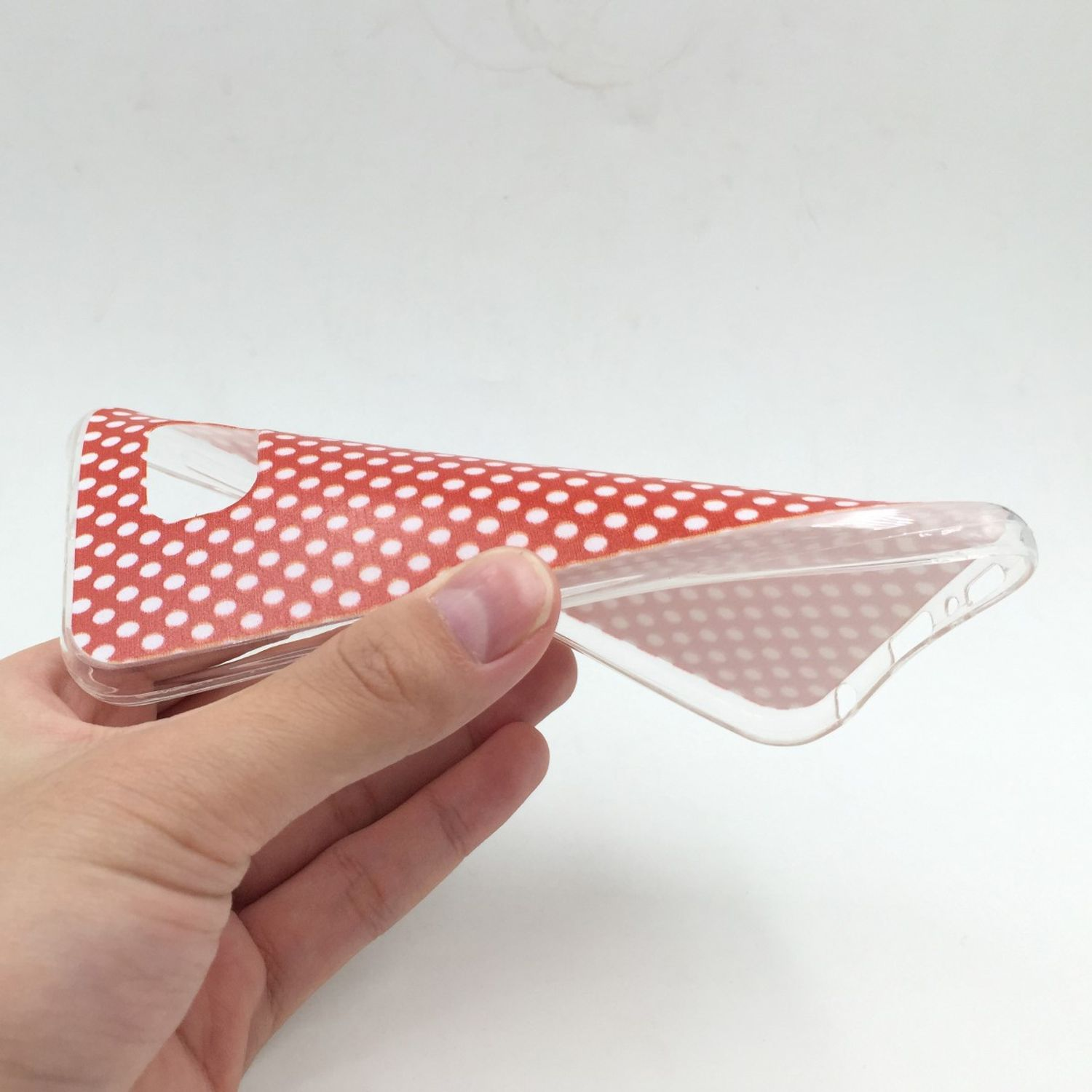 Hand hält eine Handyhülle mit weißen Polka Dots auf rotem Hintergrund, leicht gebogen.