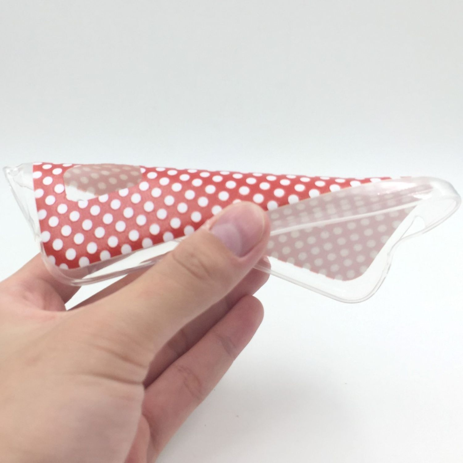 Hand hält eine rote Handyhülle mit weißen Punkten. Weißer Hintergrund und transparente Hülle.