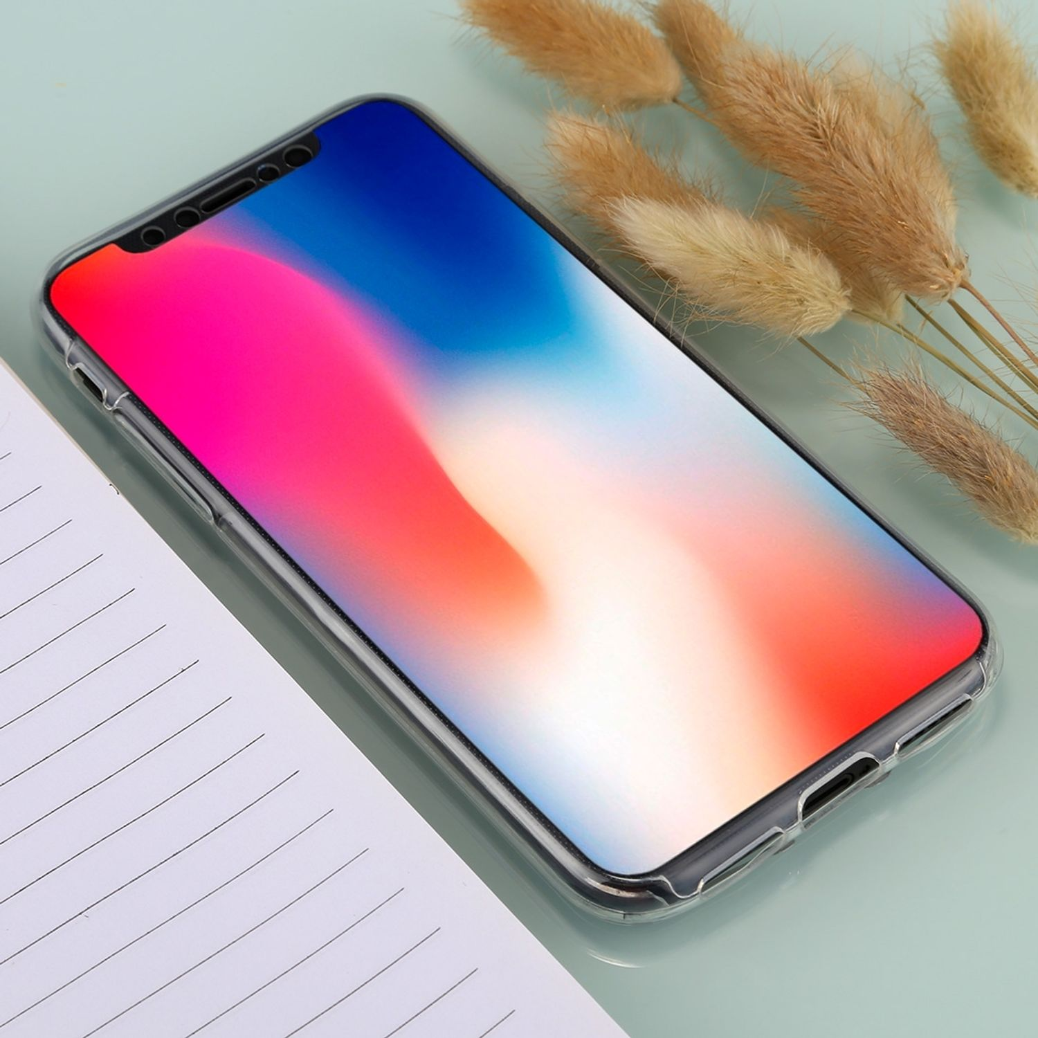 Telefon in durchsichtiger Hülle mit buntem Hintergrund. Weißes Notizbuch. Getrocknete Pflanzen.