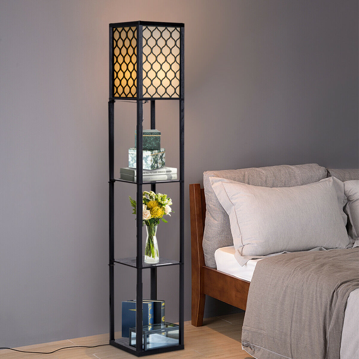 Hohe schwarze Stehlampe mit Regalen, Büchern und Blumen. Der Hintergrund ist eine graue Wand und ein Bett.