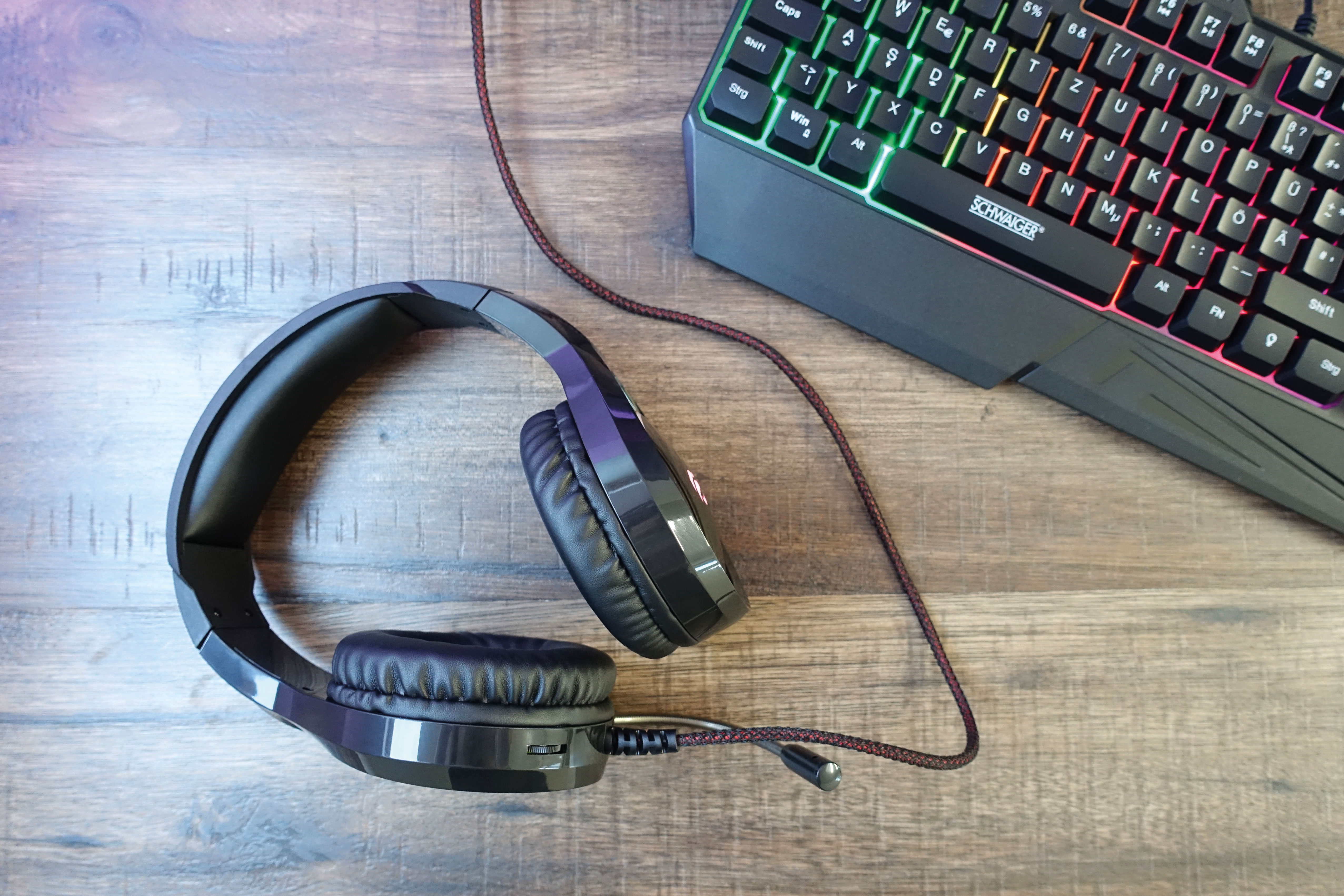 Schwarzes Gaming-Headset und eine Tastatur mit bunten Lichtern auf Holz.