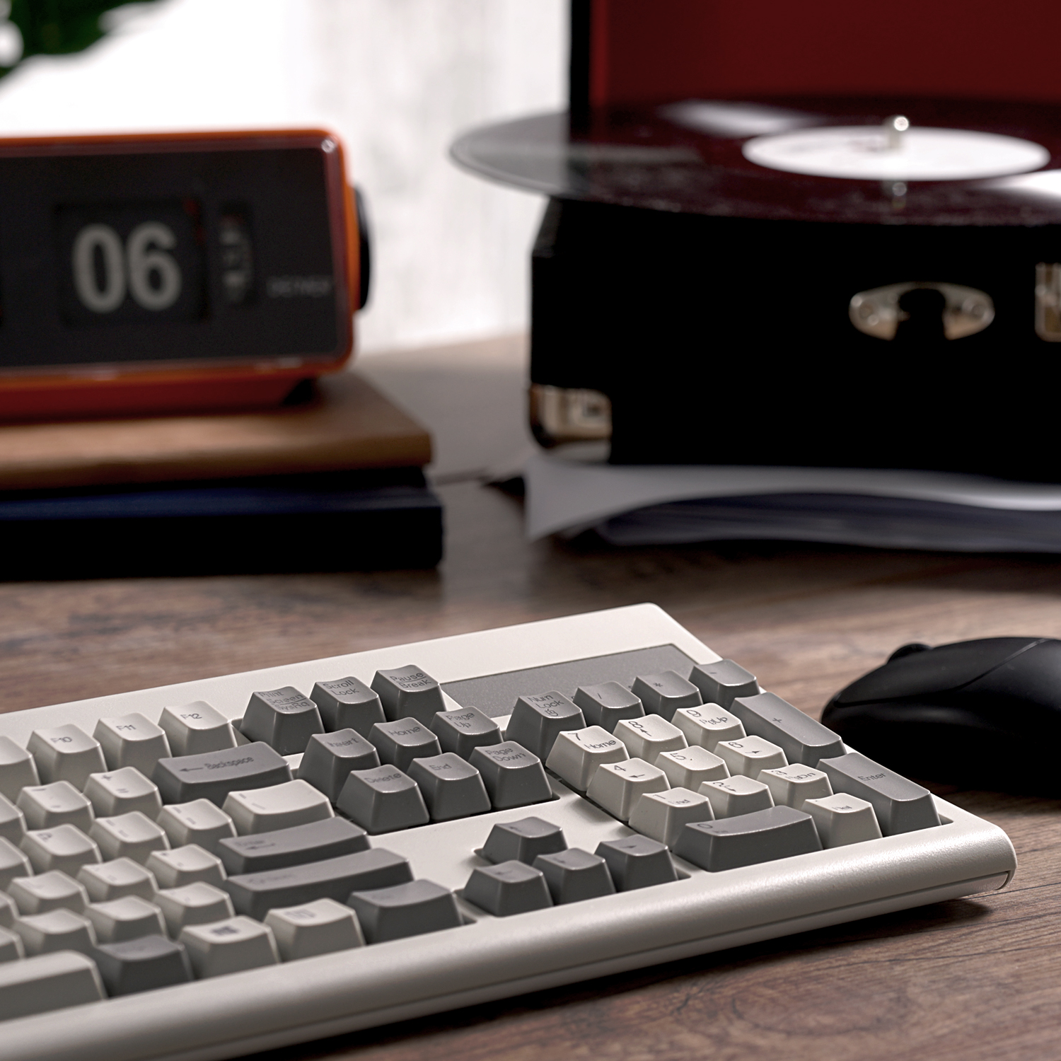Tastatur, Maus und eine orangefarbene Uhr auf einem Schreibtisch mit Plattenspieler. Holzschreibtisch.