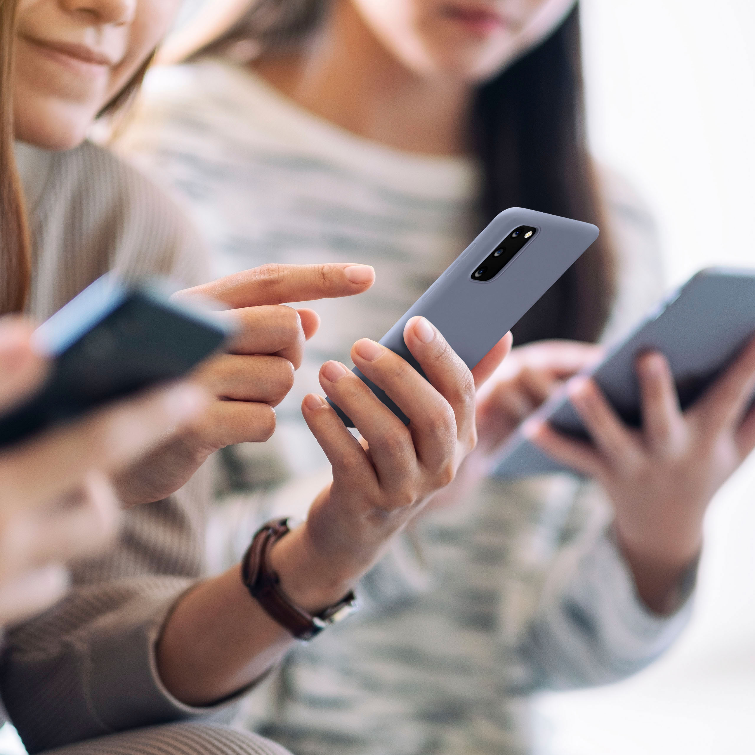 Drei Personen halten und benutzen Telefone, unscharfer Hintergrund. Fokus auf dem Telefon.